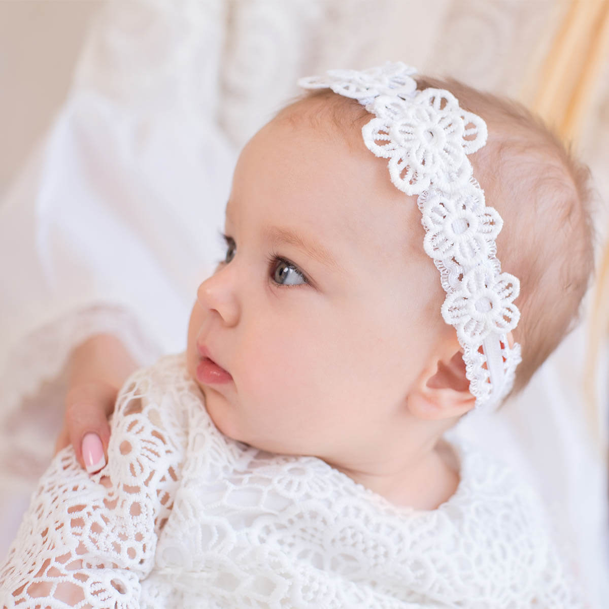 Baby wearing a white lace headband and outfit on a soft background