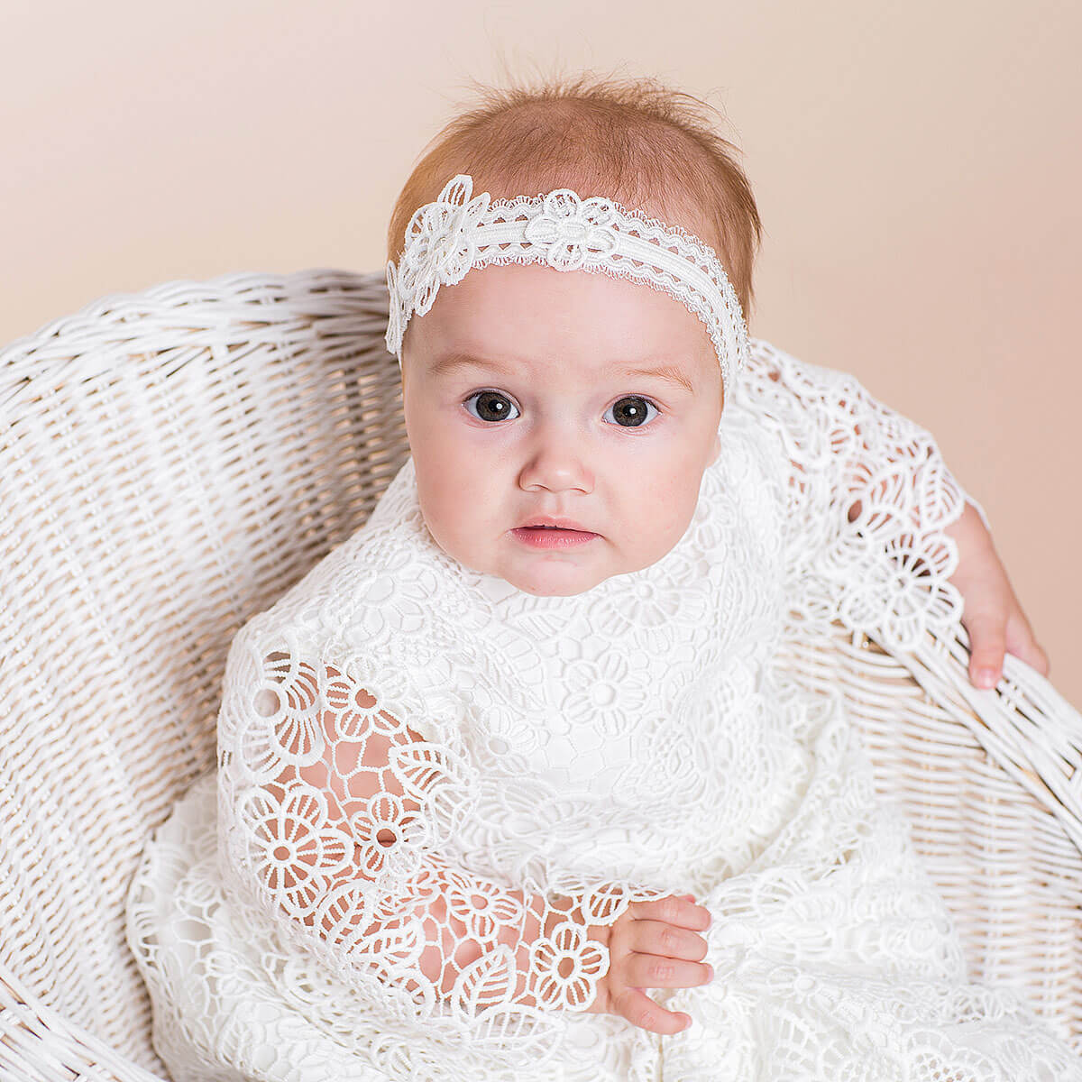 Baby wrapped in a white lace blanket and headband against a beige background