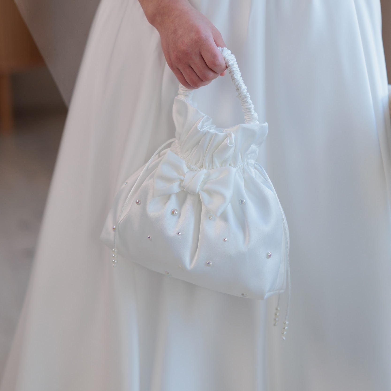 White lace handbag communion accessories held by a person wearing a white dress.