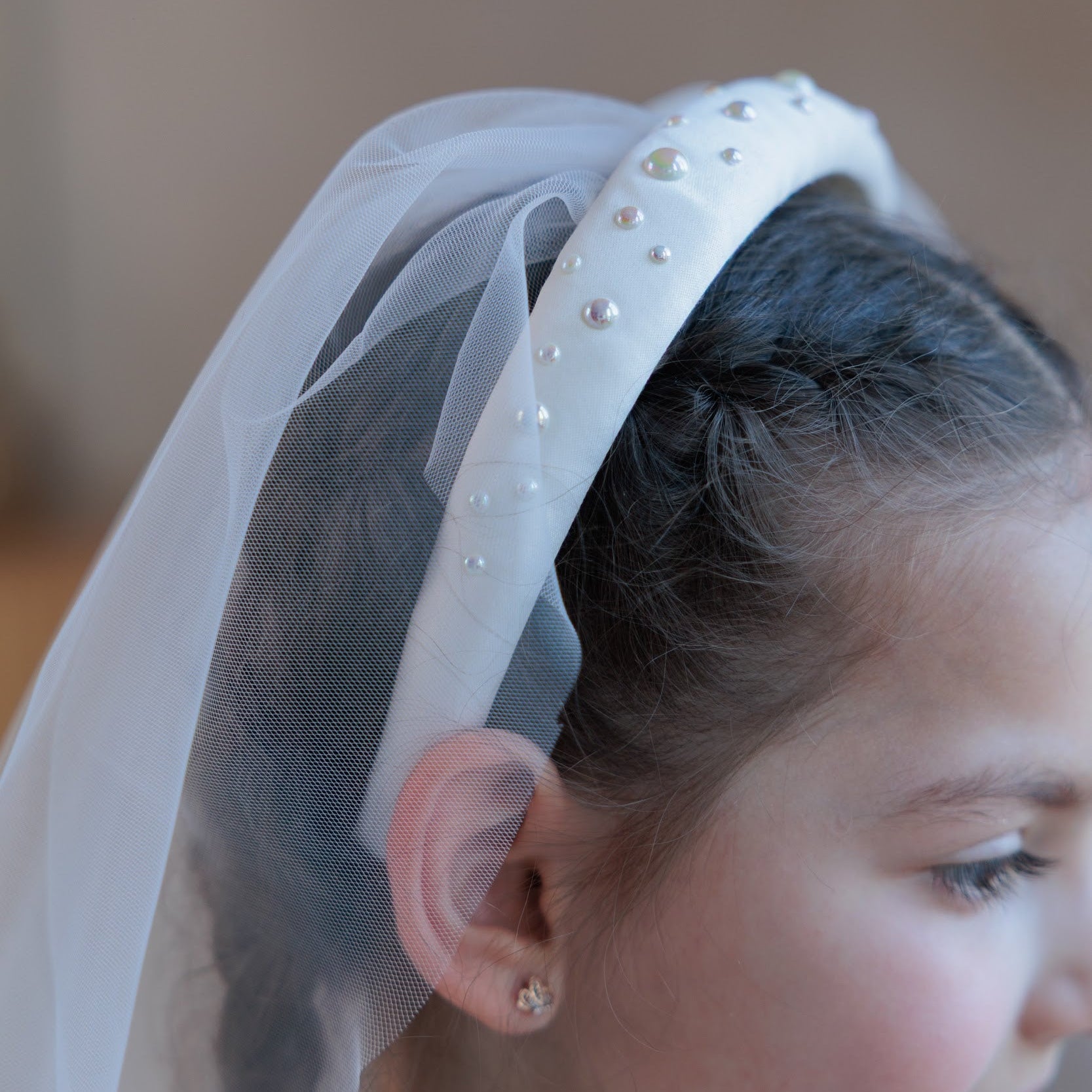 Close-up of a young girl wearing a white headband with pearls and a small communion veil.