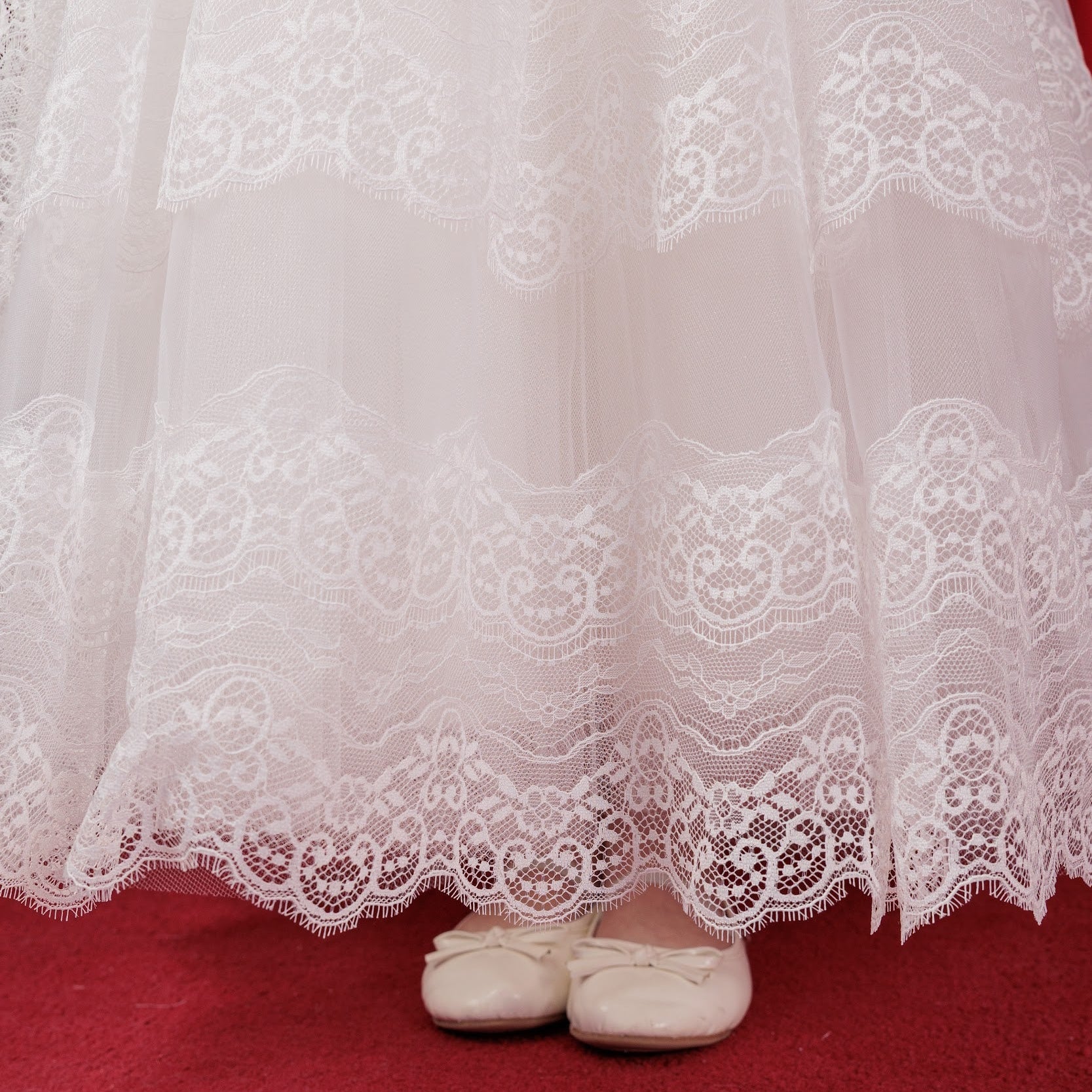 White lace-trimmed dress on a red carpet with white shoes visible