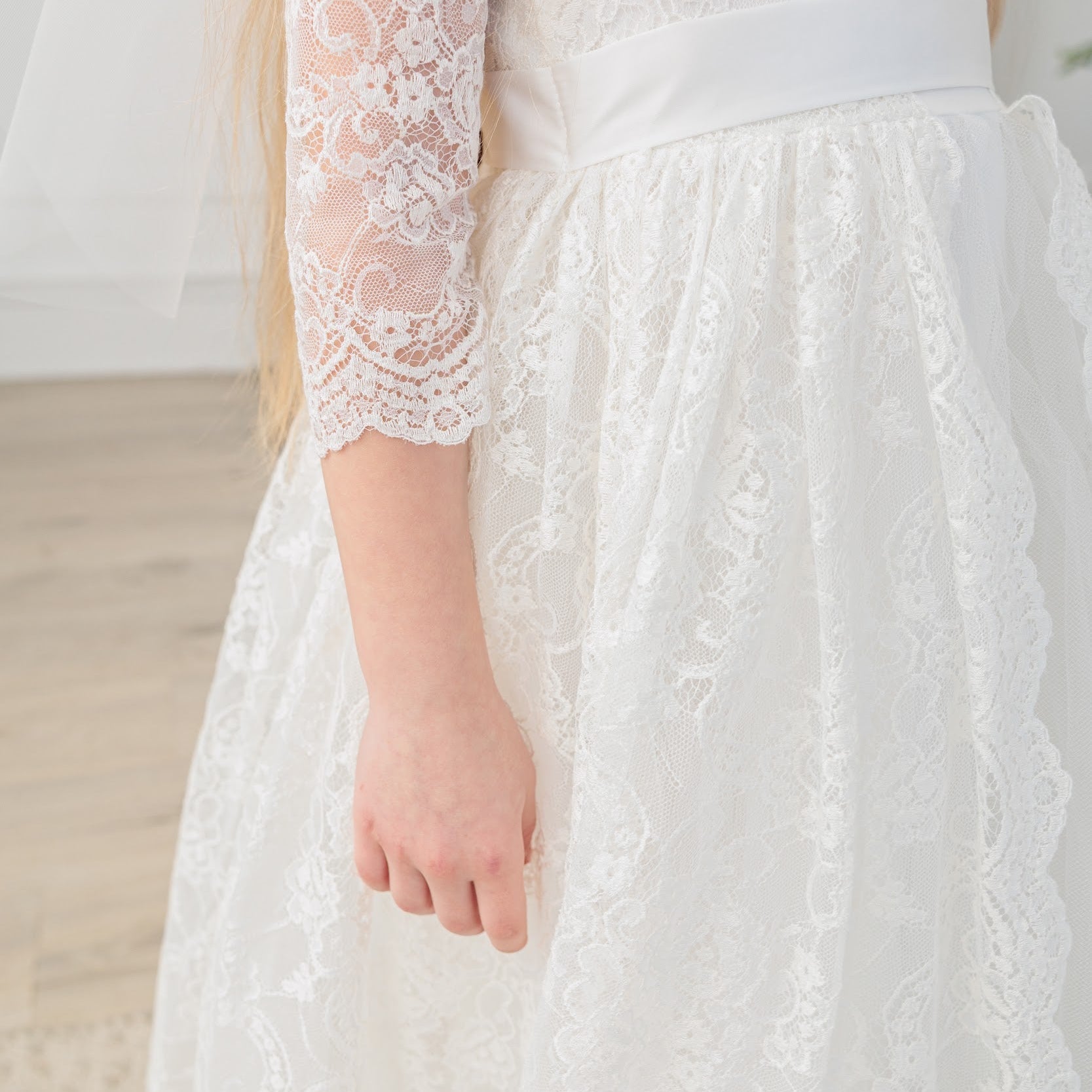 Close-up of an ivory lace communion dress with long sleeves.
