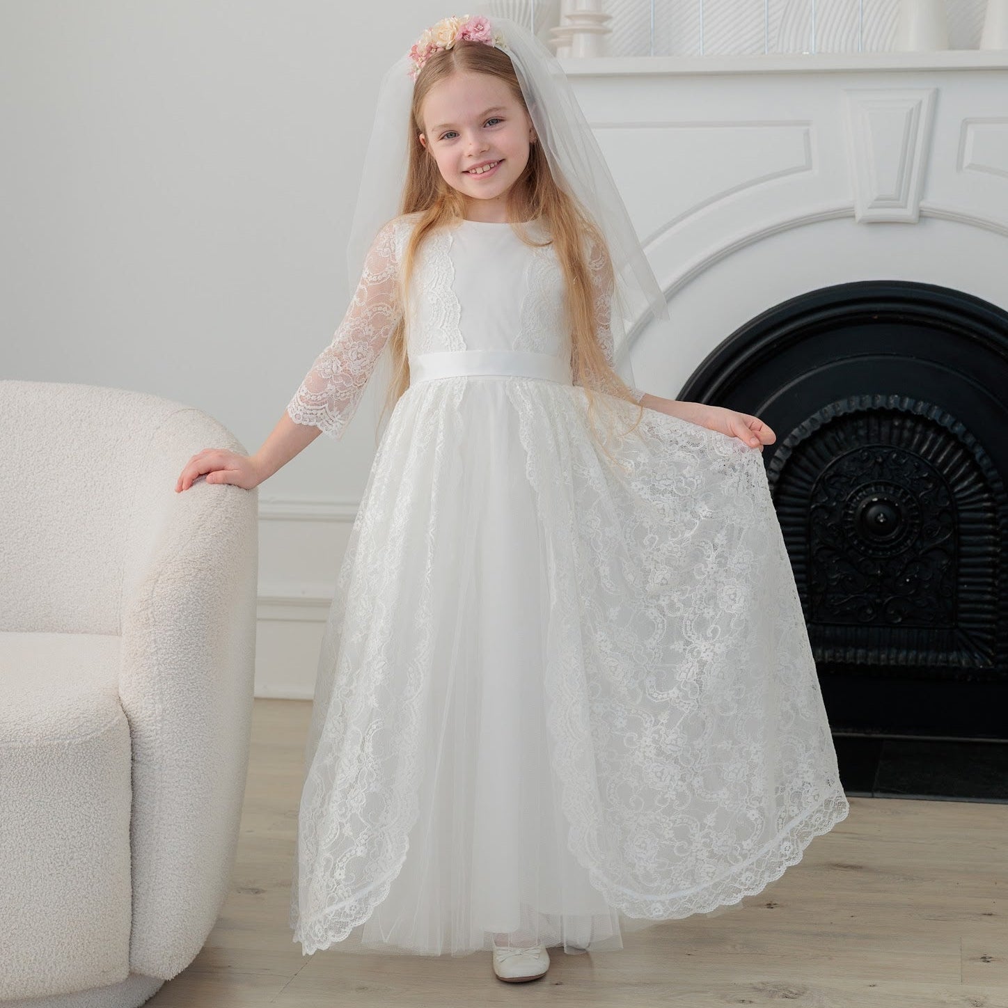 Young girl in an ivory lace communion dress standing in a room with a fireplace.