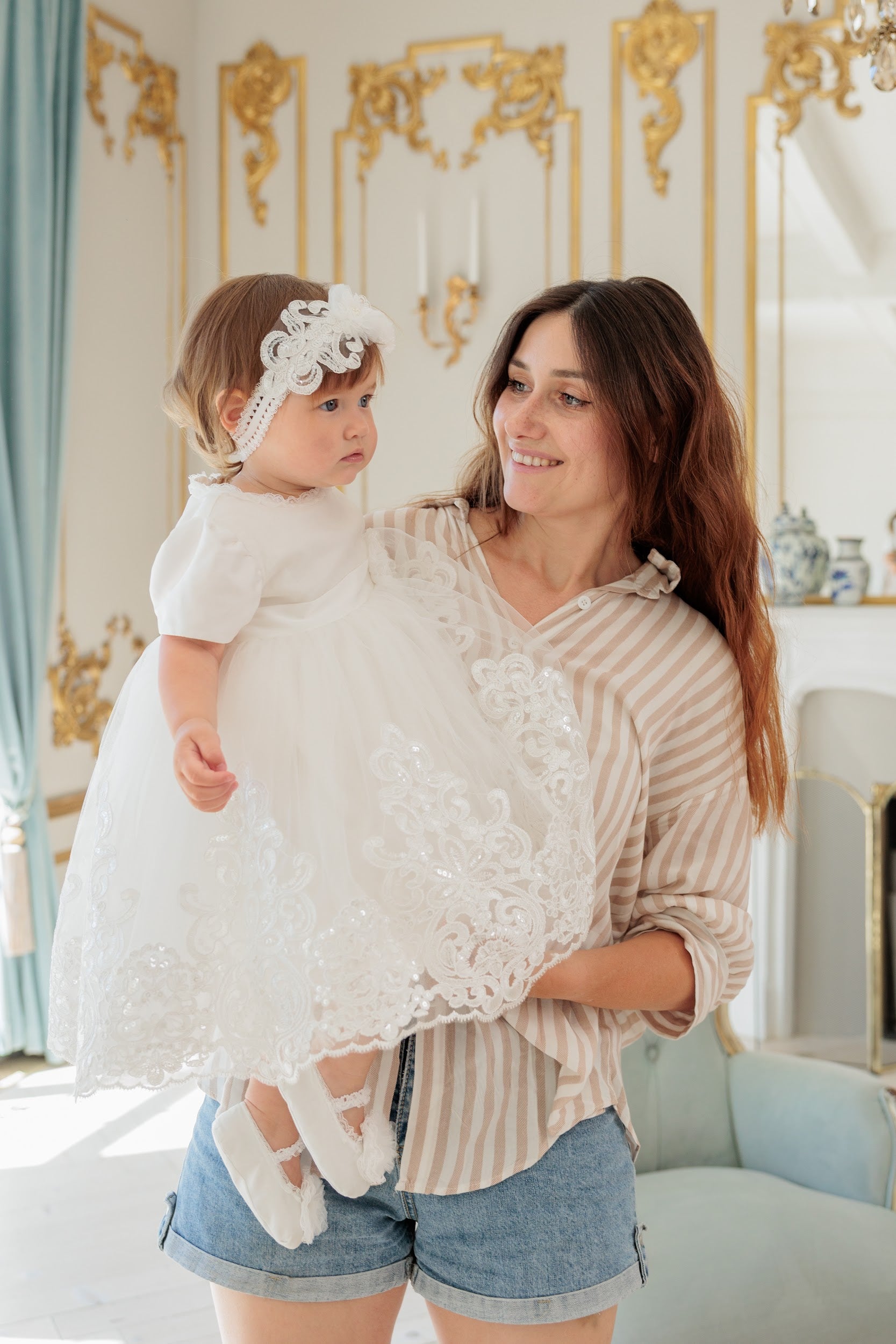 The baby is wearing a white baptism lace dress and headband