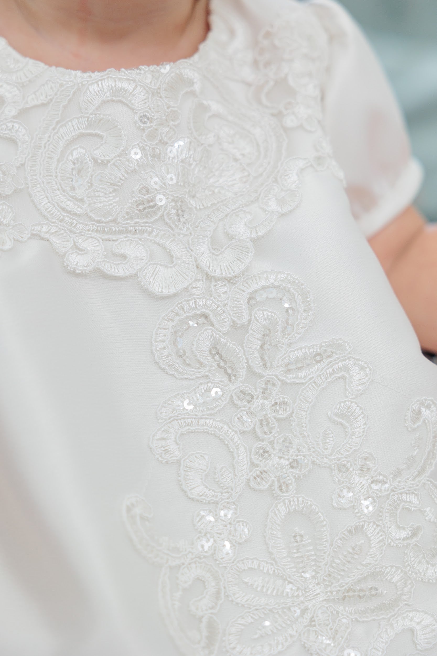 Close-up of a white short-sleeve dress with ornate lace embroidery and sequined floral detailing on the chest and bodice.