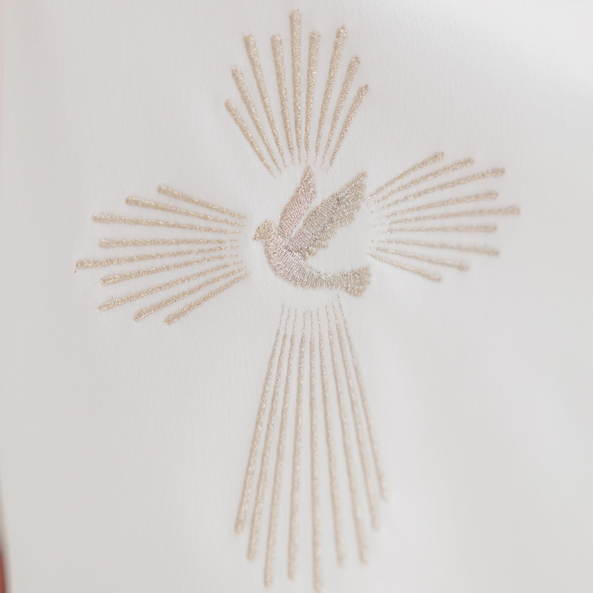 A close-up of a white fabric featuring a metallic gold embroidered cross with a central dove of light.