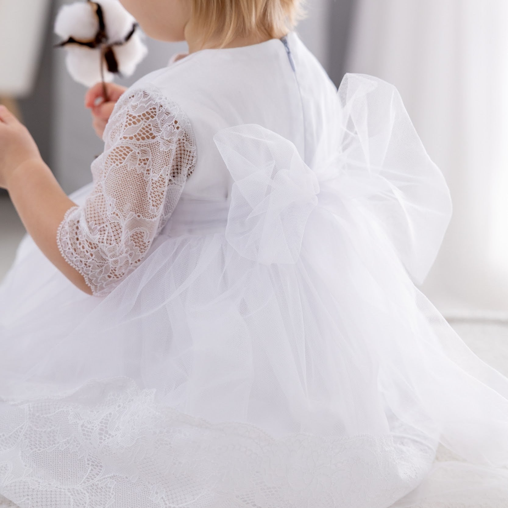 Child wearing a white lace dress sitting on a light-colored surface.
