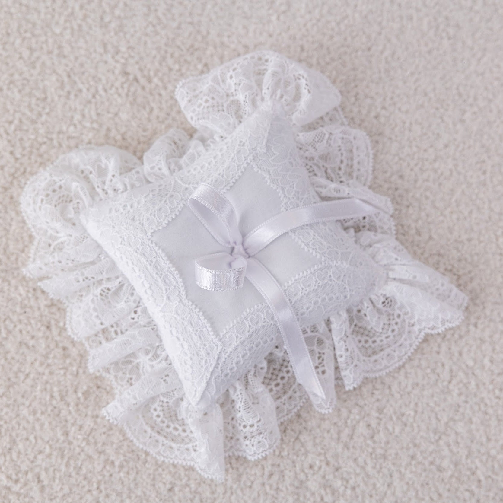 White lace ring pillow with a bow on a beige surface