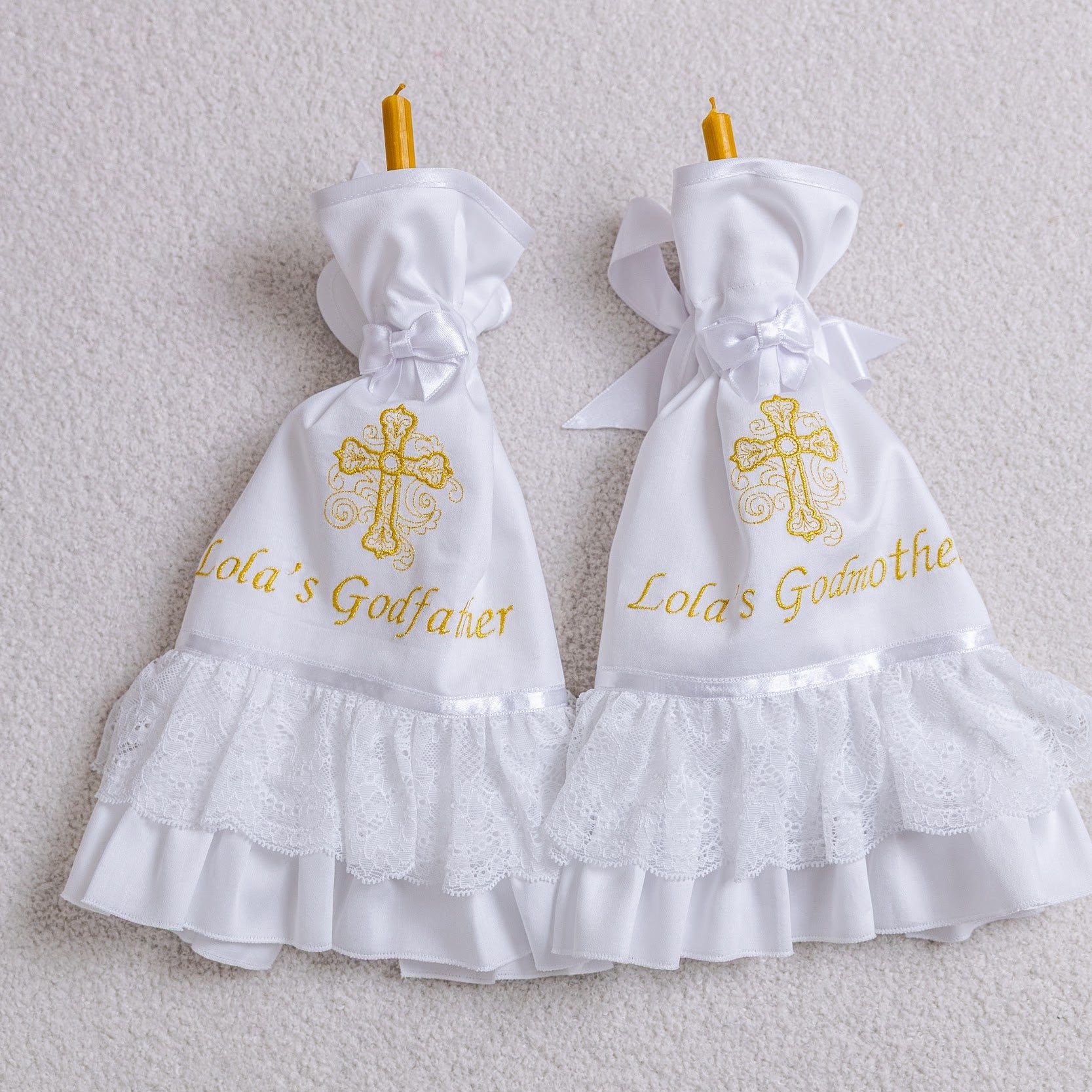 Two white baptism candle wraps with ruffles and embroidered crosses on a light gray background