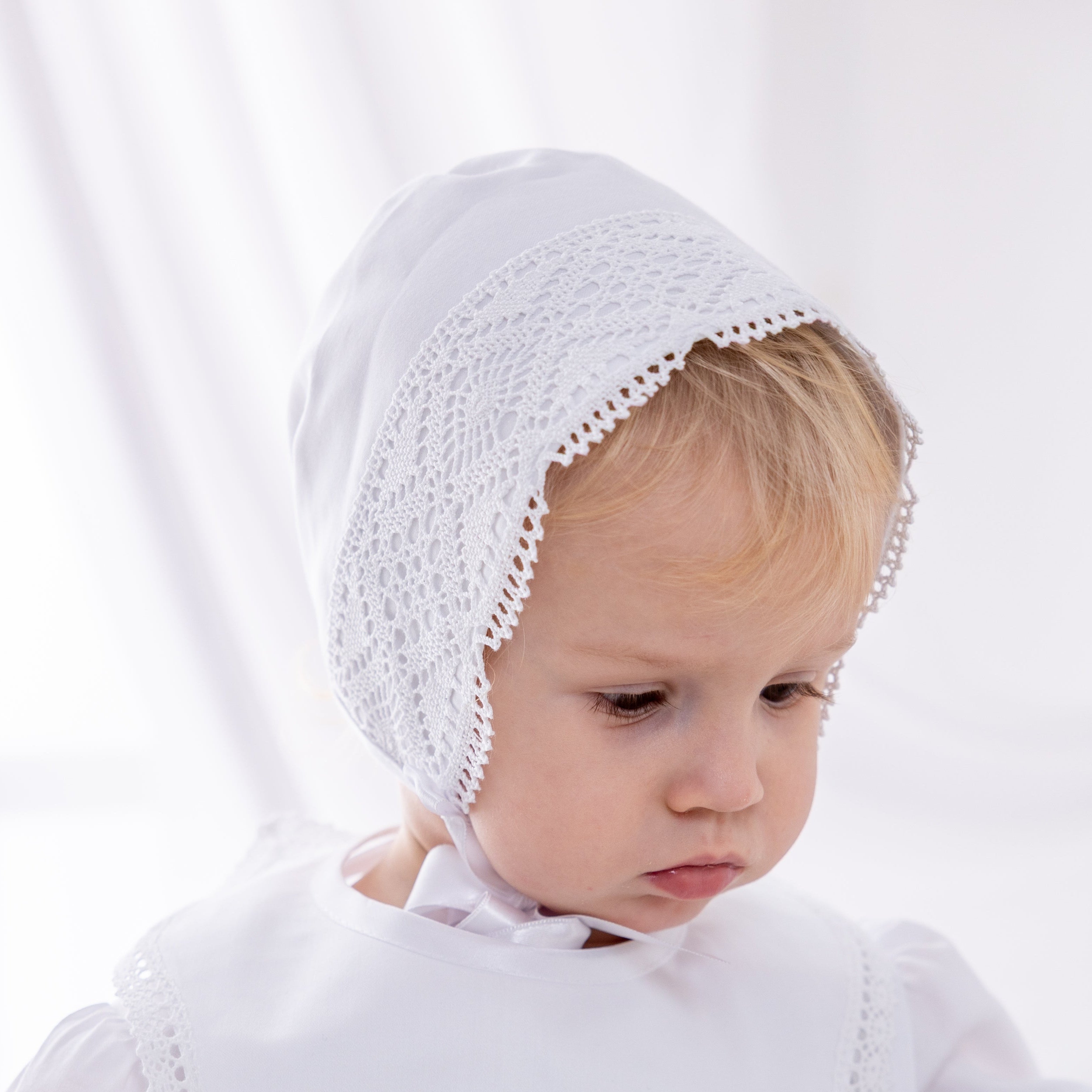 Baby wearing a white embroidered bonnet and bib on a white background