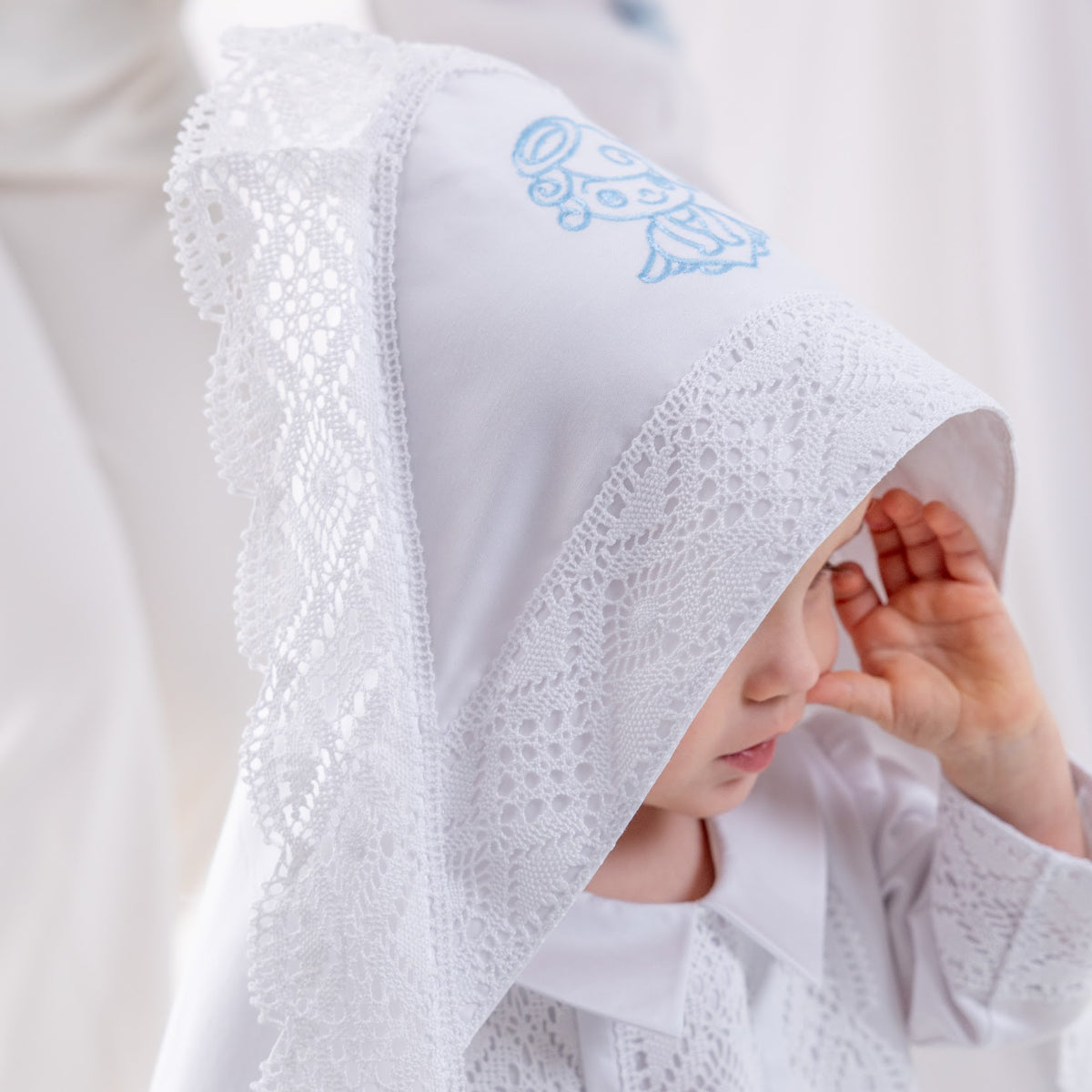Child wearing a white baptism blanket with a blue angel