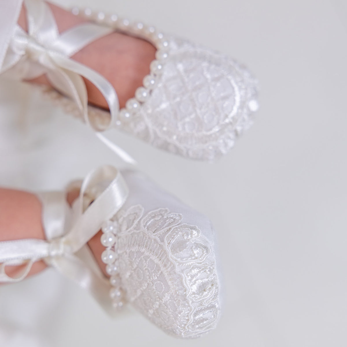 Christening Booties with lace and pearl details on a light background