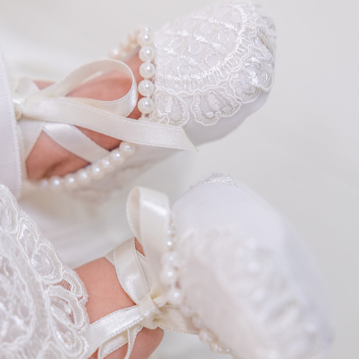 Christening Booties with ribbons and pearls on a white background