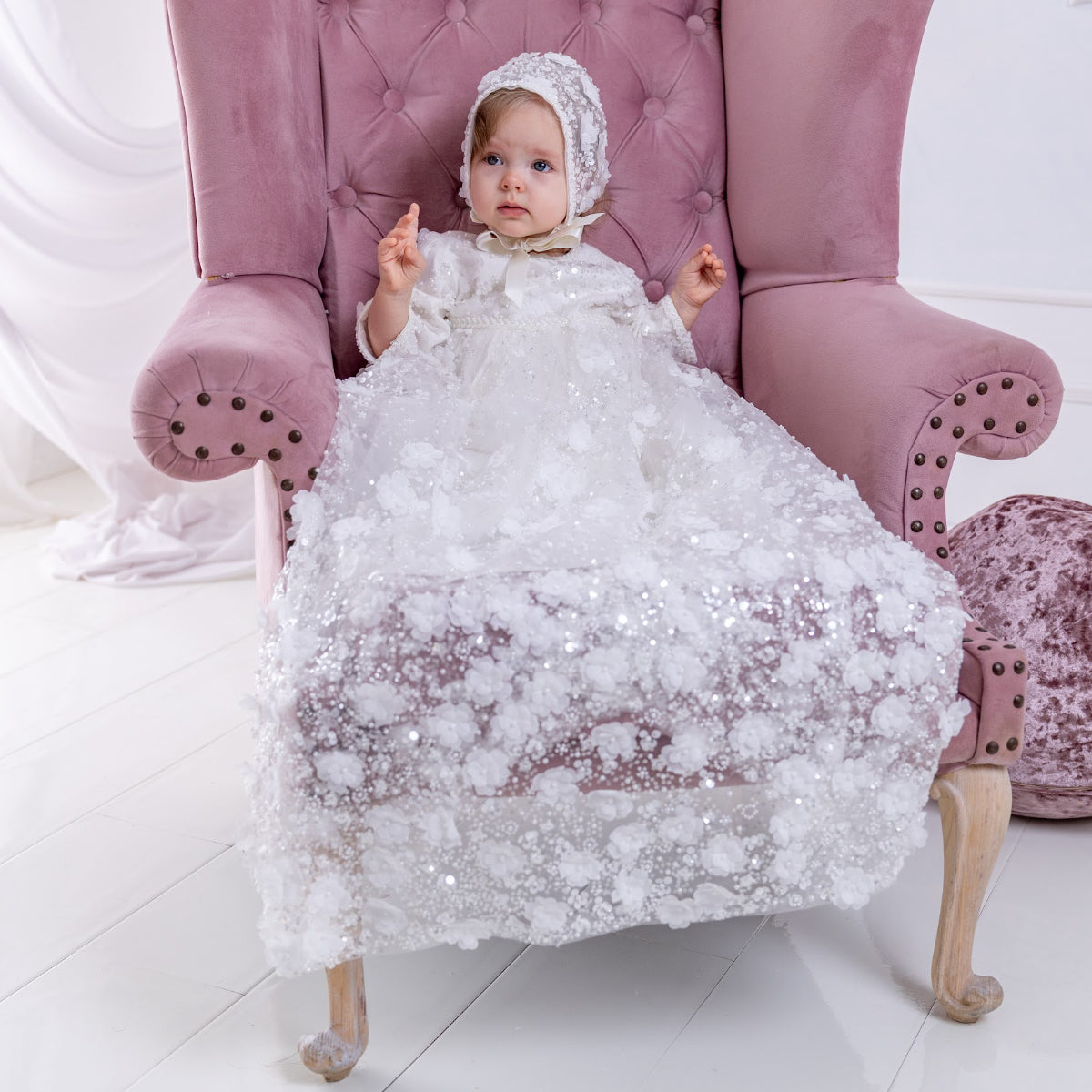Baby in a heirloom christening gown sitting on a pink chair