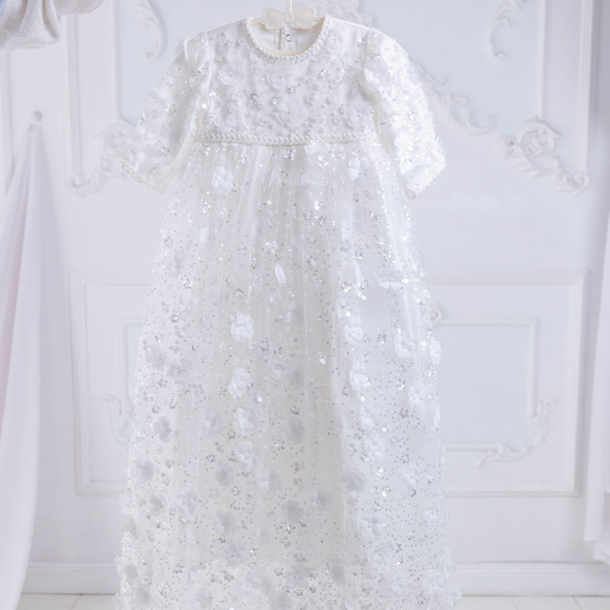 Heirloom christening gown on a hanger against a white wall