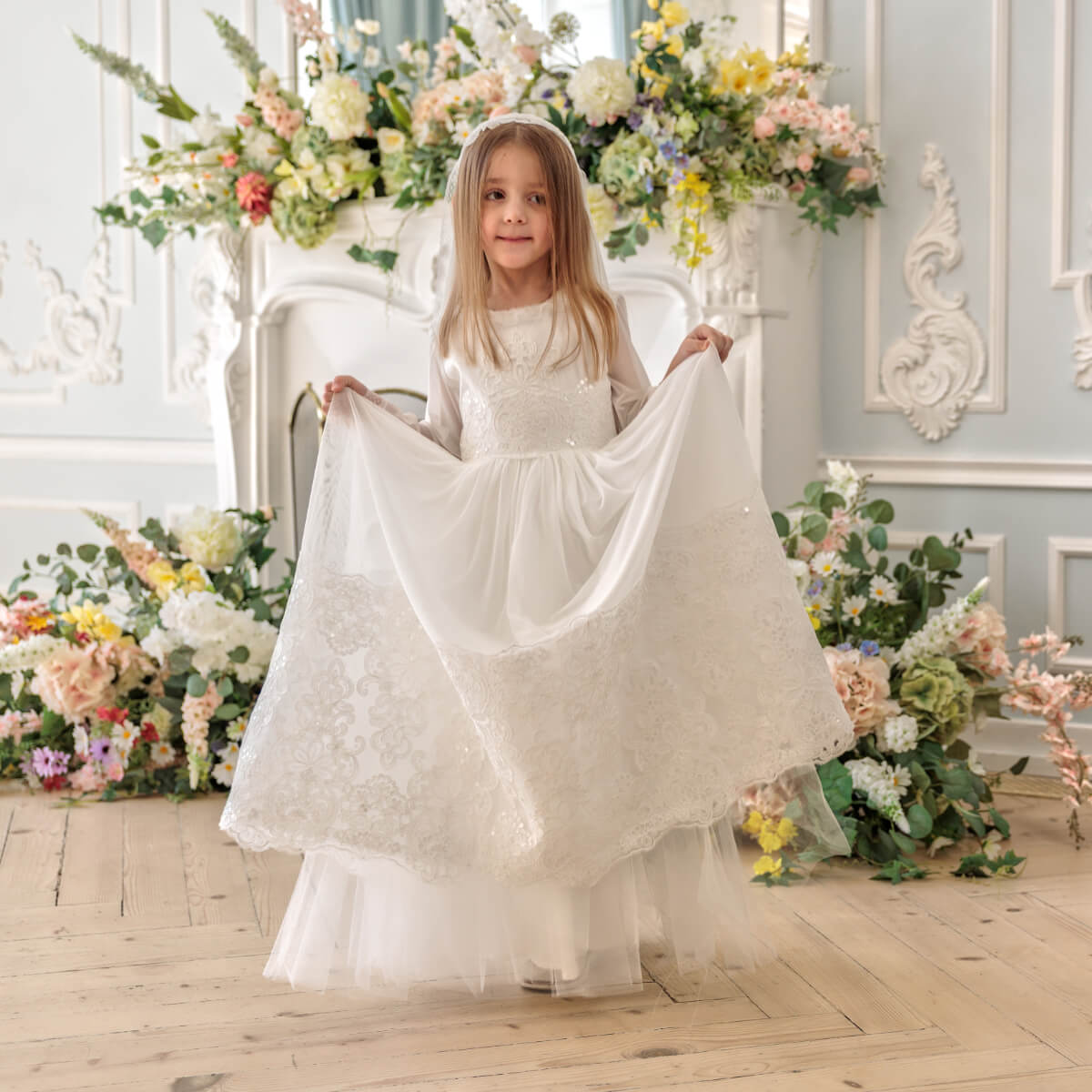 Young girl in Holy Communion Dress standing in a decorated room with floral arrangements.