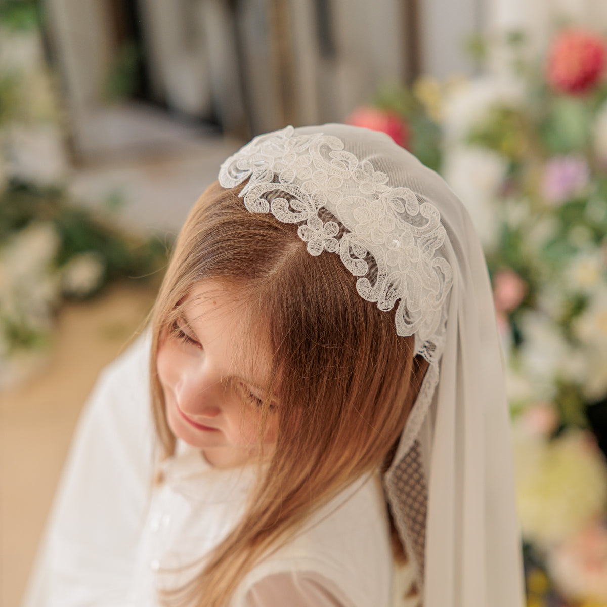 Young girl wearing a white lace headband and veil with a blurred floral background
