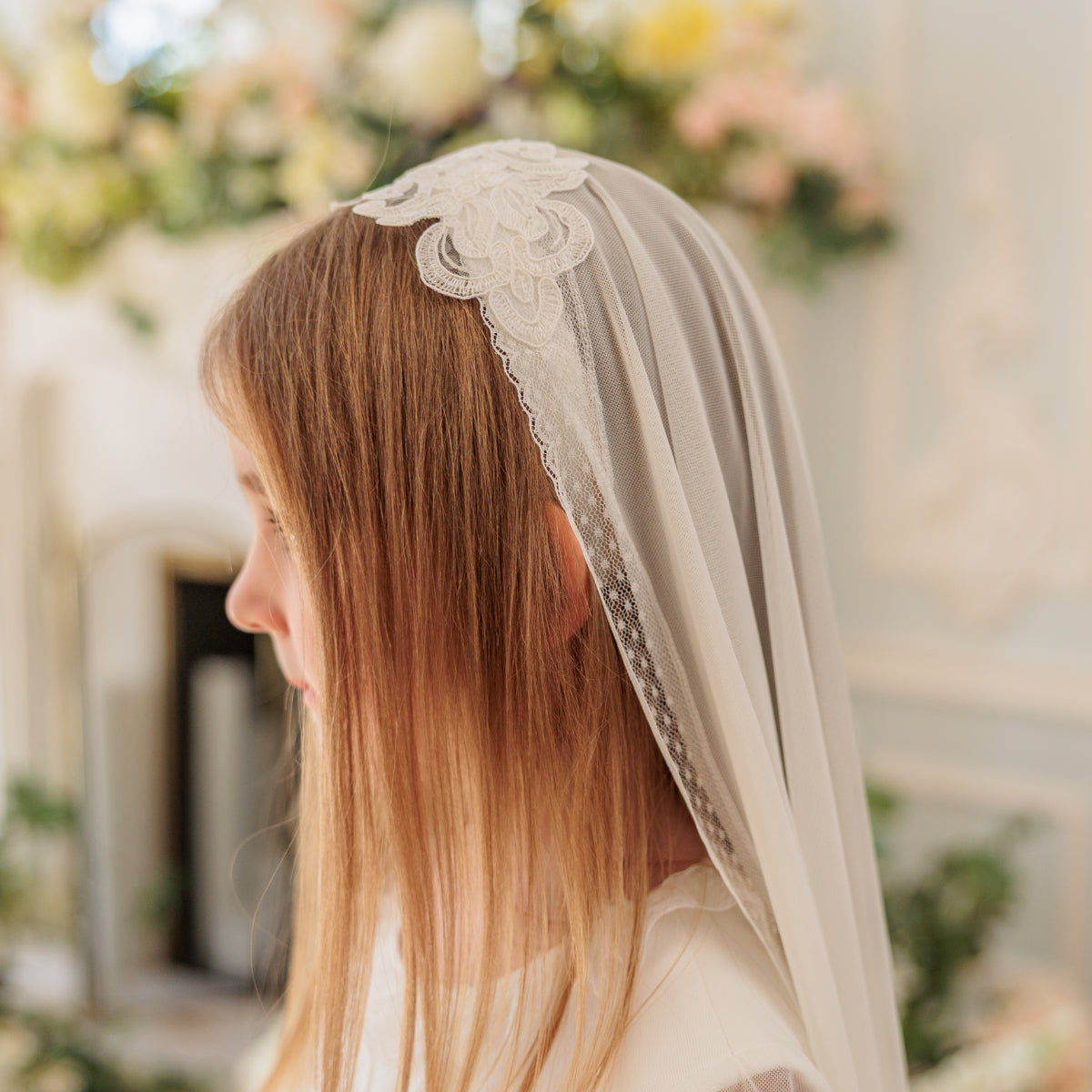 Woman wearing a lace veil with a blurred floral background