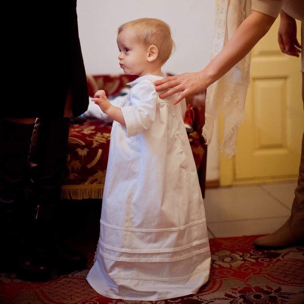 Child in a white robe being helped by an adult in a home setting