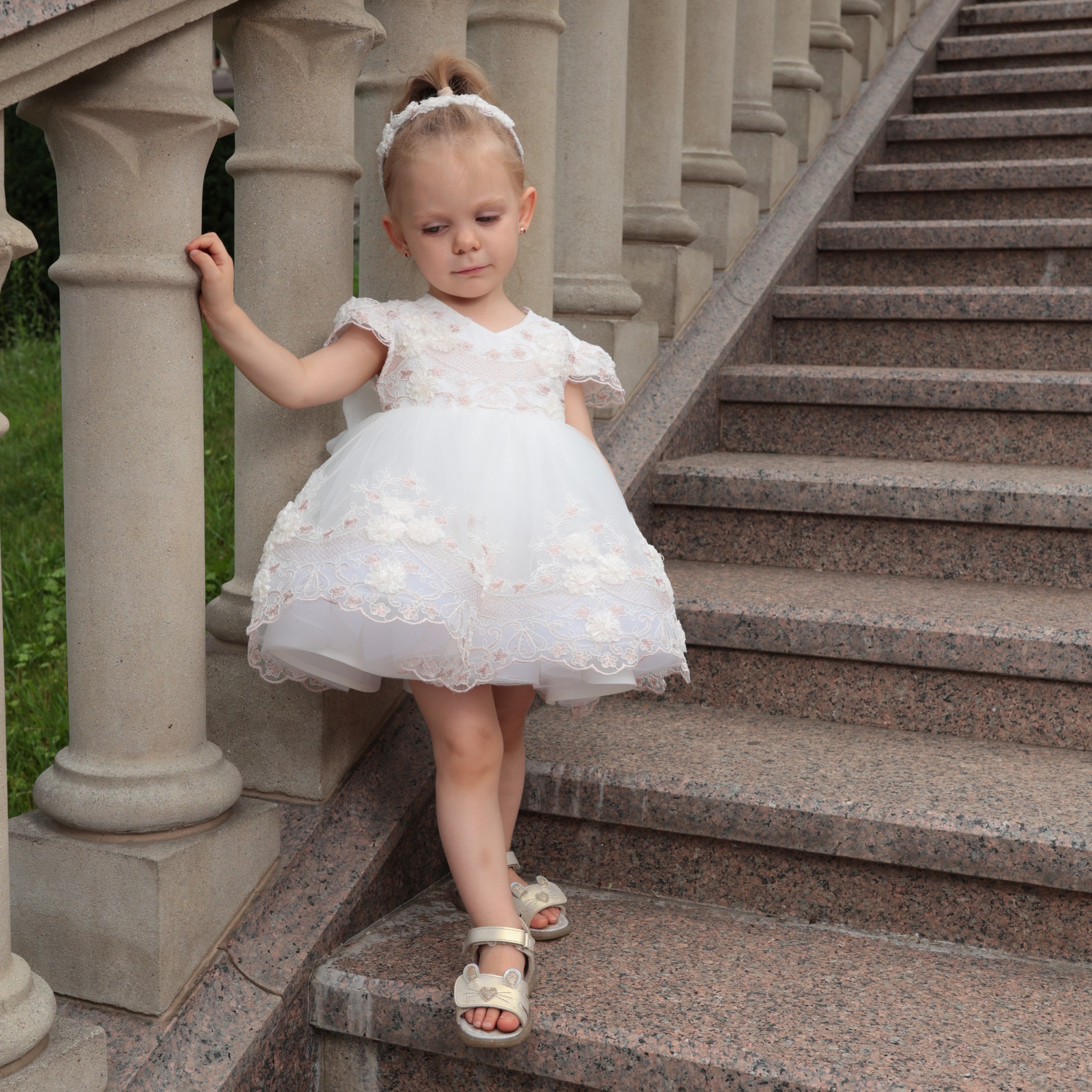 Young girl in a white dress standing on stone steps with columns in the background