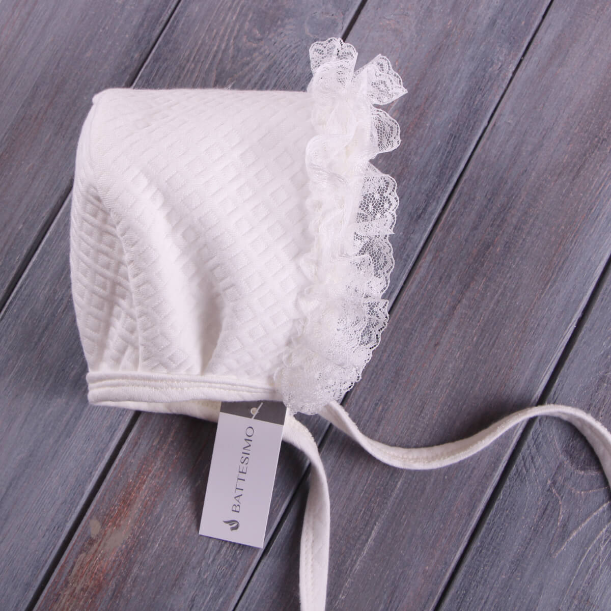 Lace Baptism Bonnet on a wooden surface, featuring the Battisimo brand.
