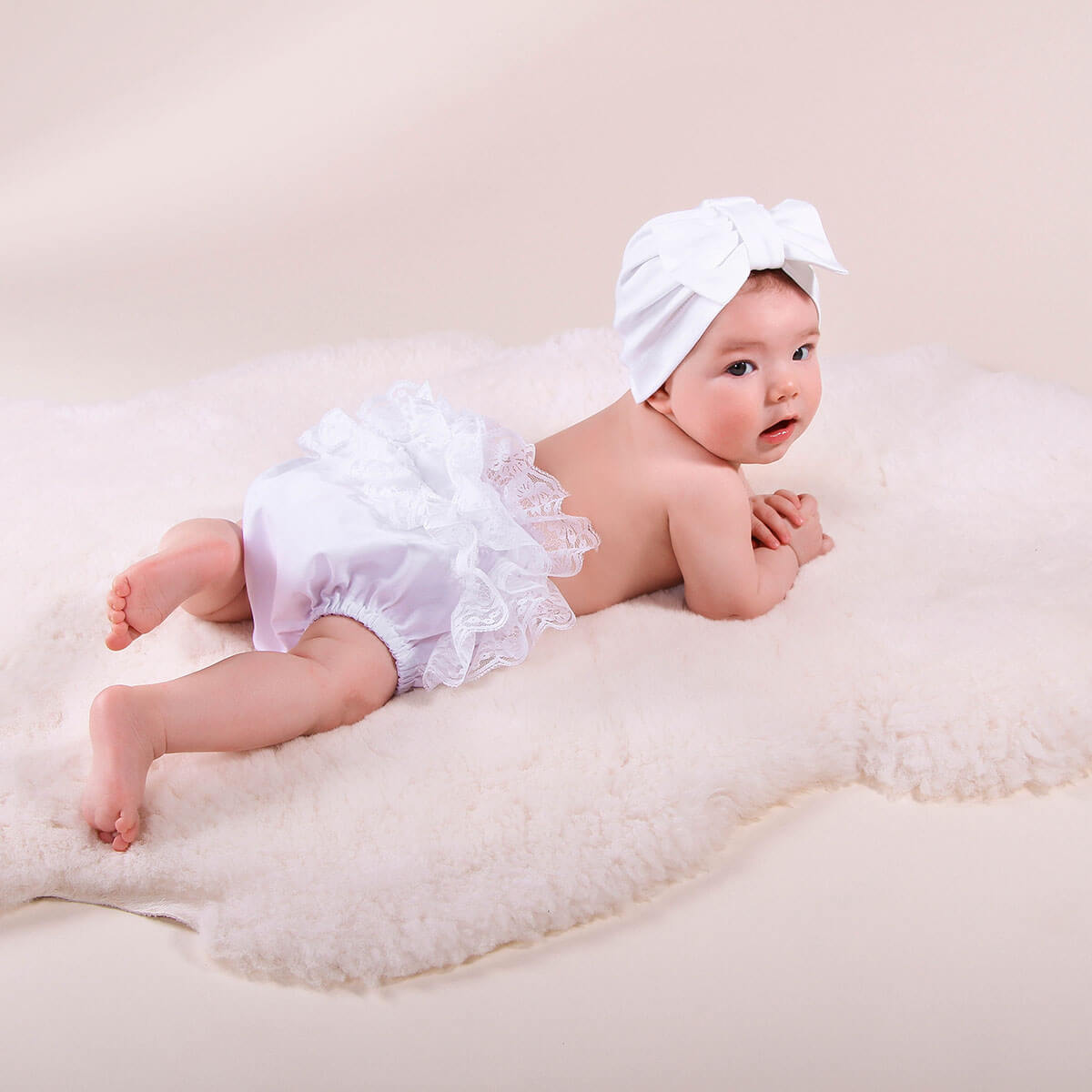Baby in a Baby Keepsake Bloomers with a bow on a beige background