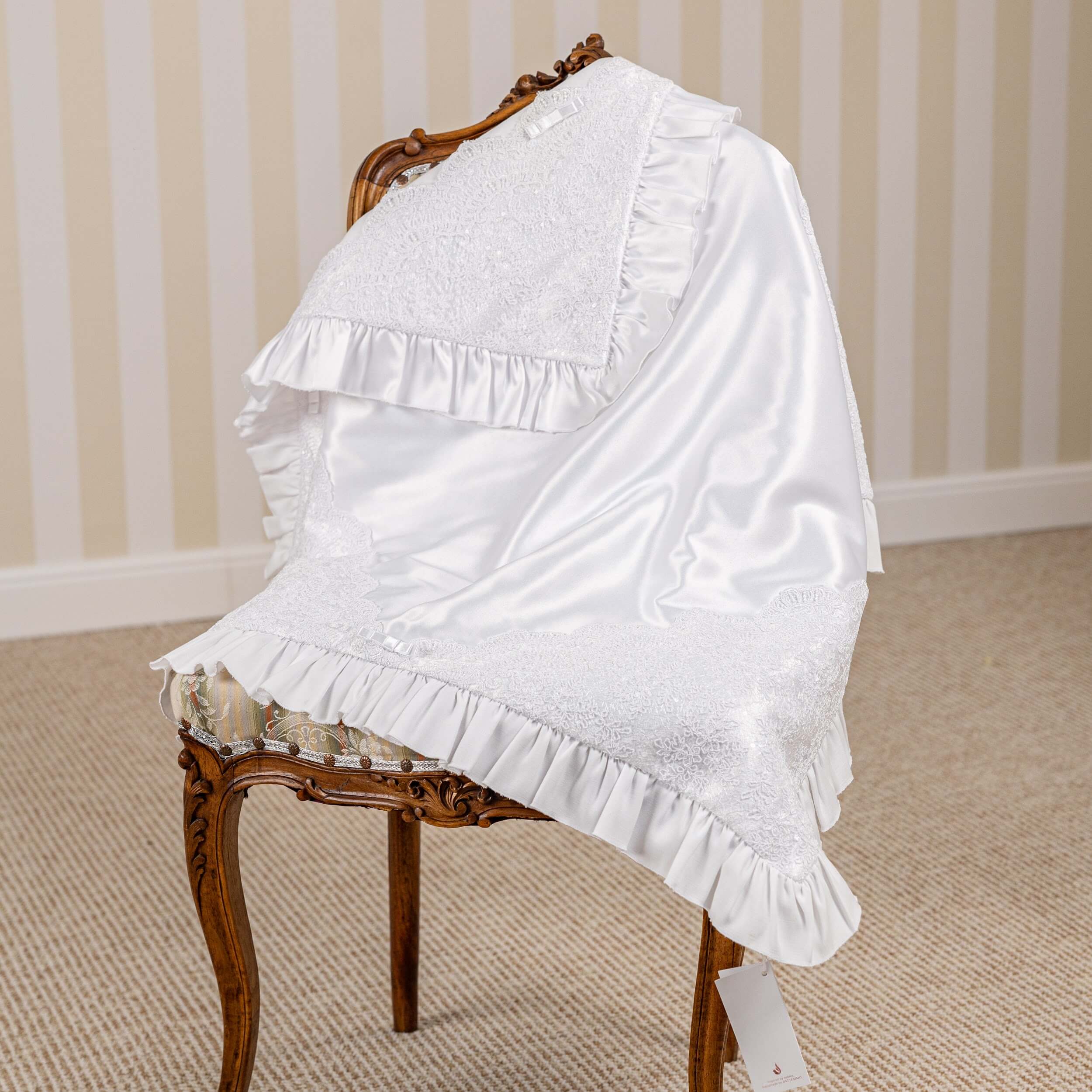 White lace baby blanket on a wooden chair against a striped wall.