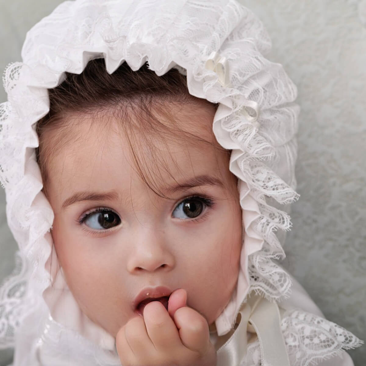 Child wearing a Lace Baptism Bonnet against a neutral background