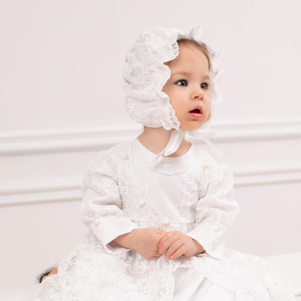Baby in a Girls Christening Gown with a bonnet against a plain background