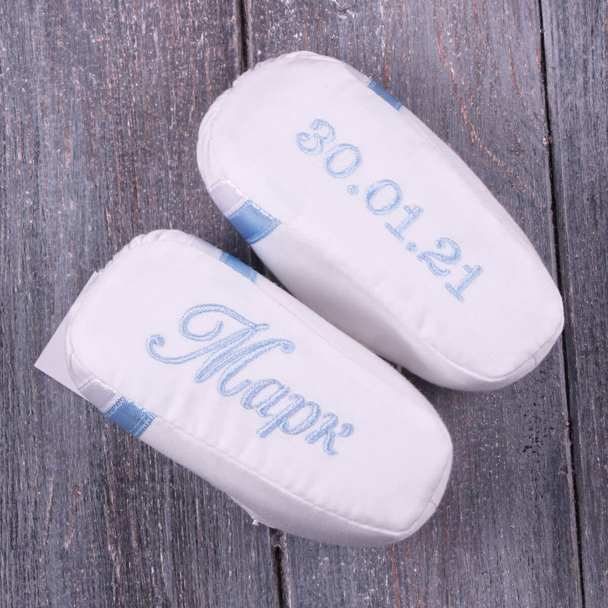 Two whiteWhite baptism booties with blue text on a wooden surface