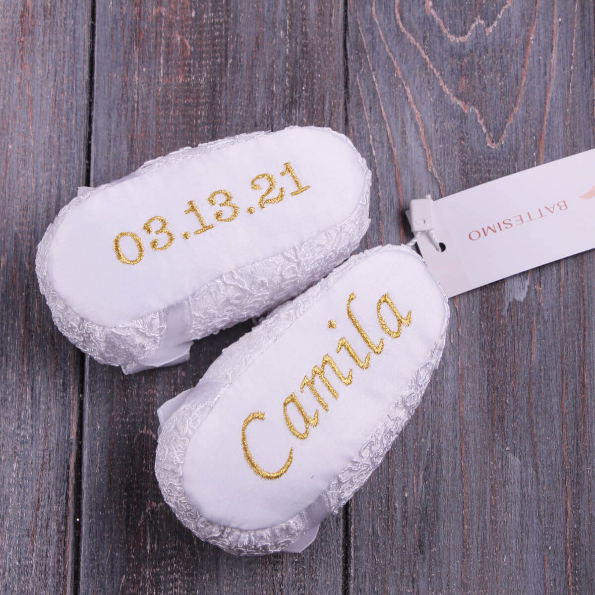 White baptism booties with gold text on a wooden surface