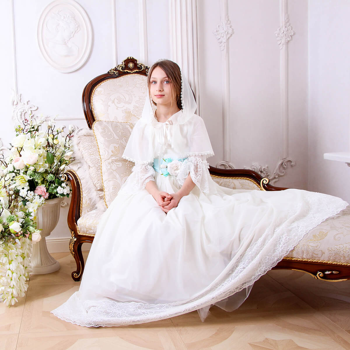 Woman in a Traditional Communion Dress sitting on an ornate chair in a decorated room.