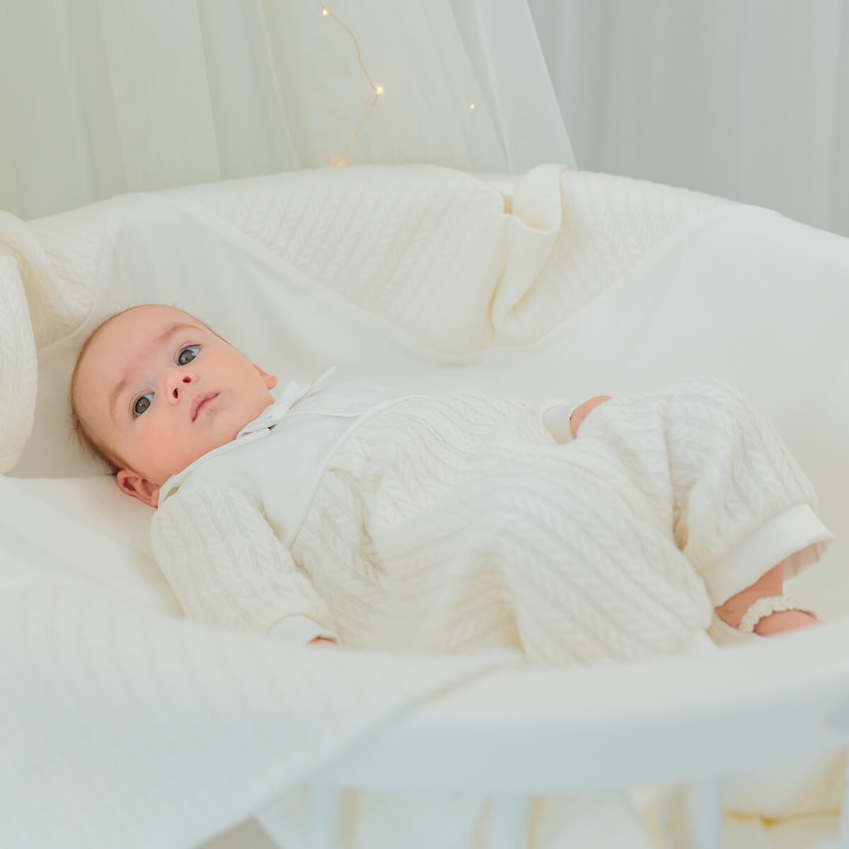 Baby wrapped in a white blanket with a soft texture, lying on a white surface.