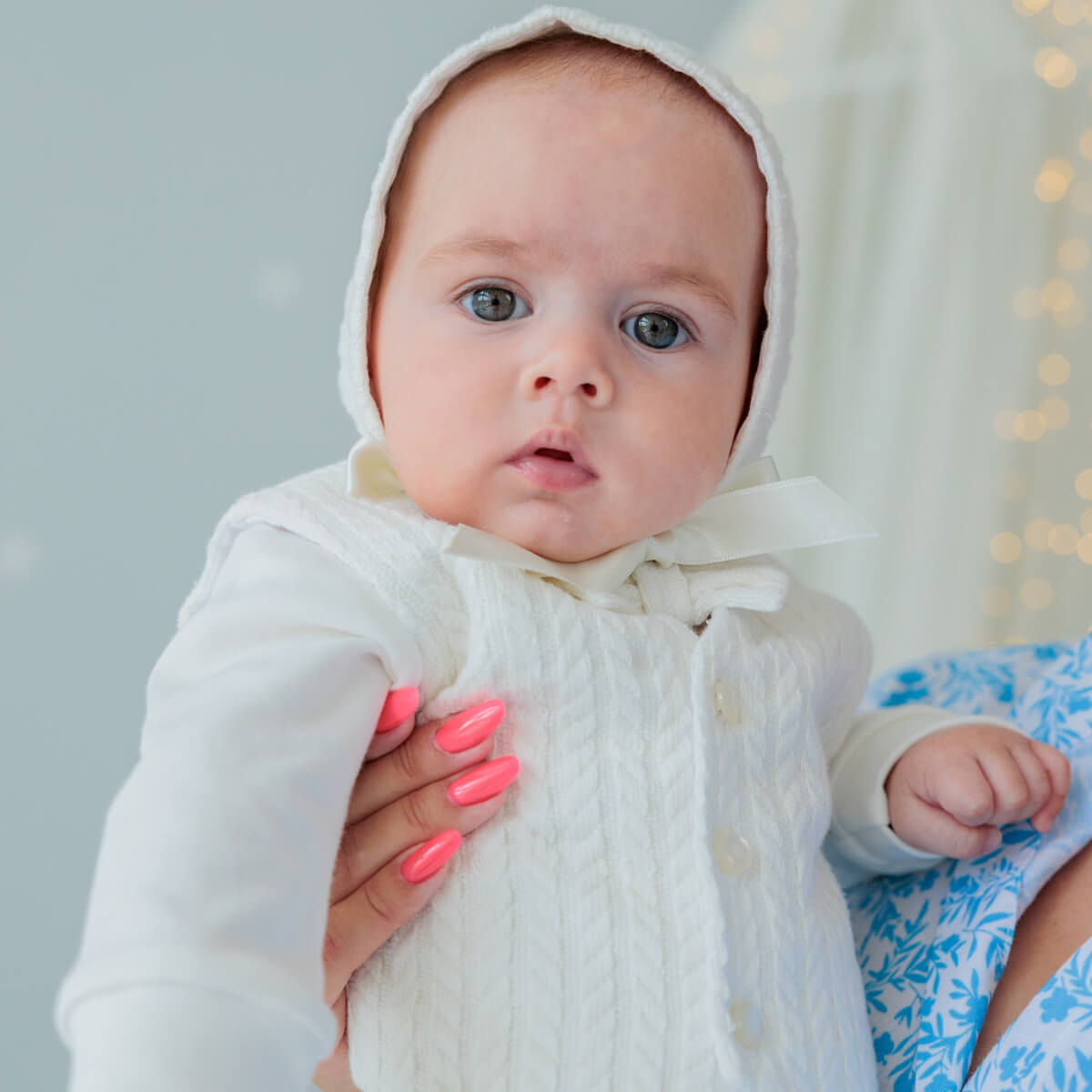 Baby in a Coming Home Jersey Outfit held by a person with pink nails against a neutral background