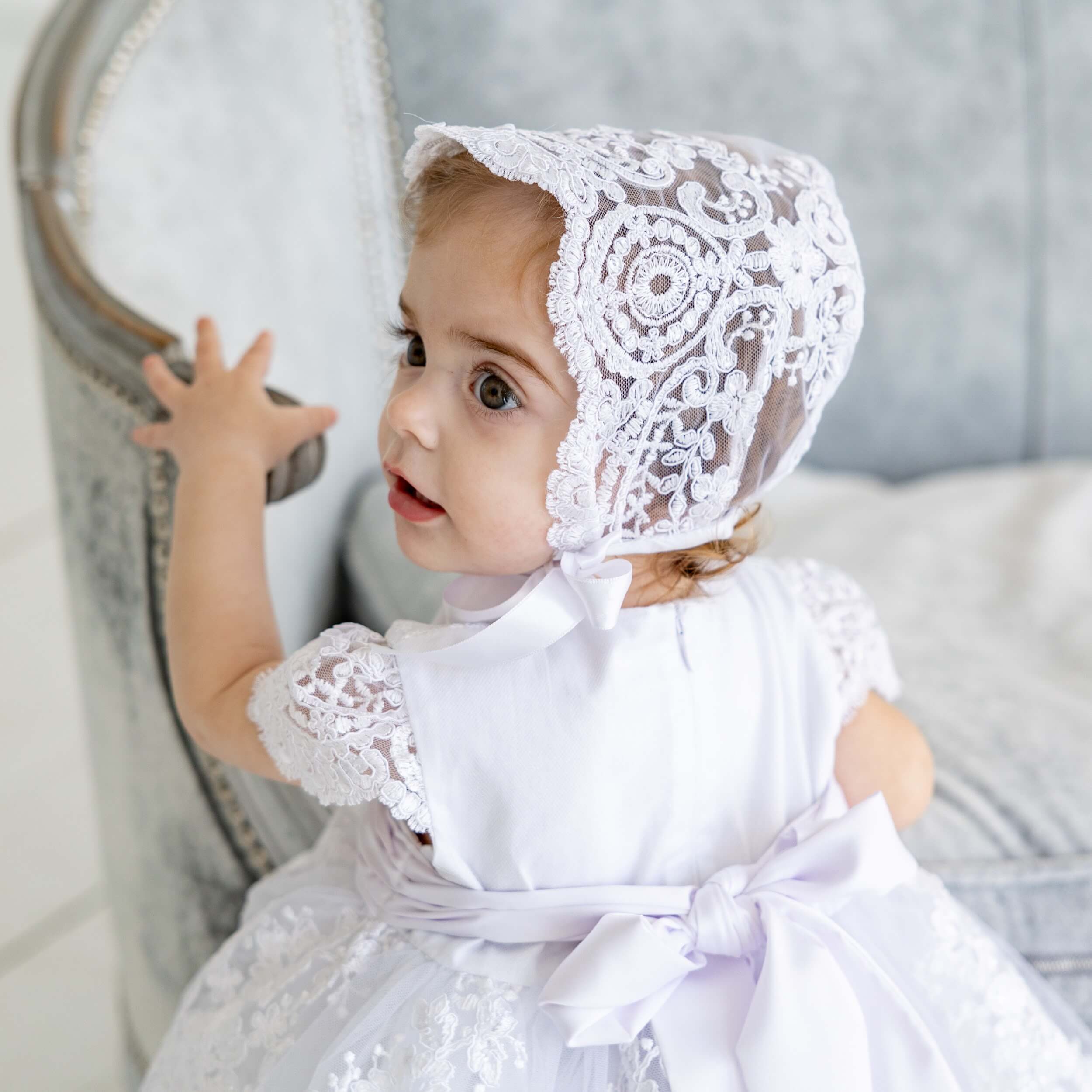 Child wearing a aLace Baptism Dress, sitting on a couch.