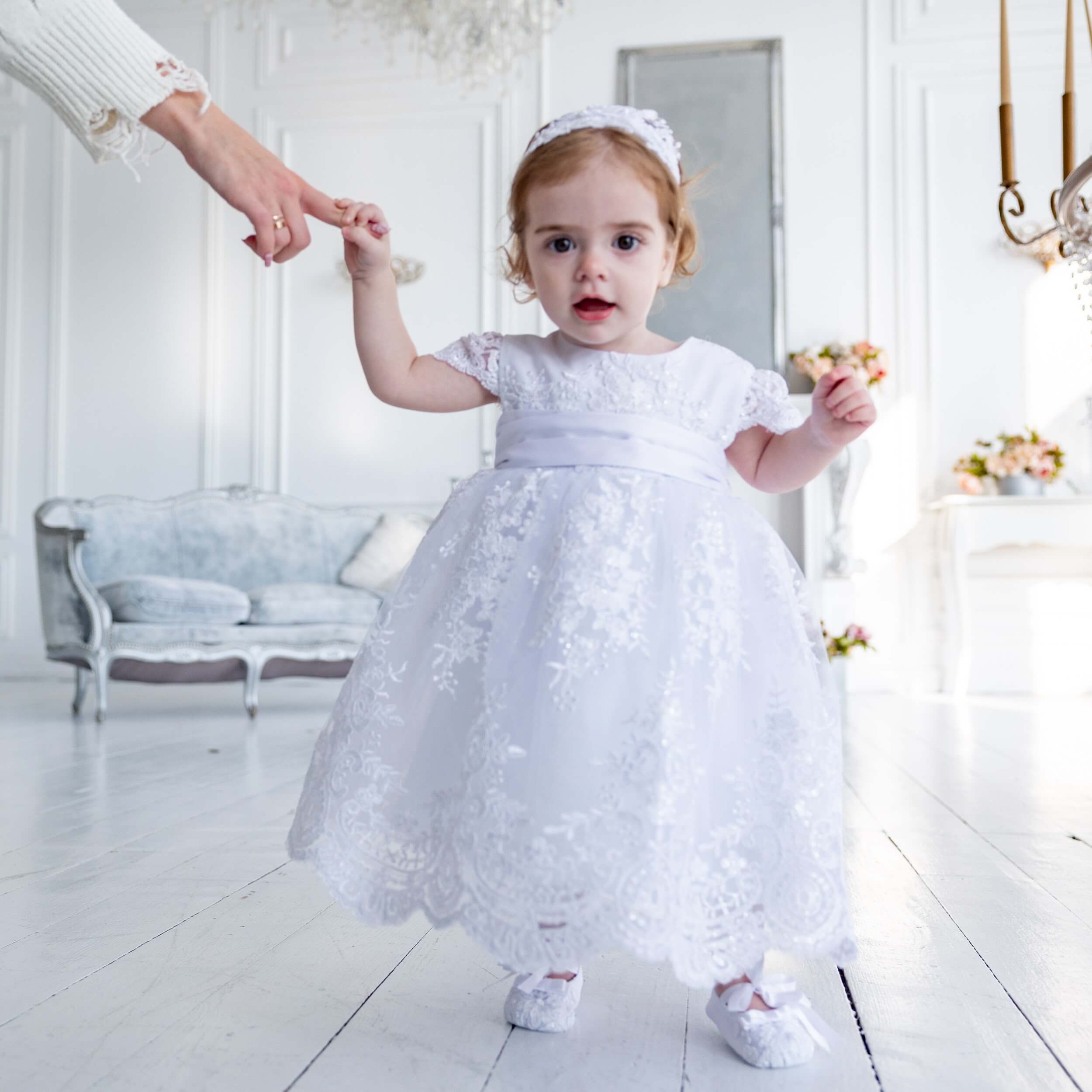 Child in a Lace Baptism Dress standing in a bright, elegant room.