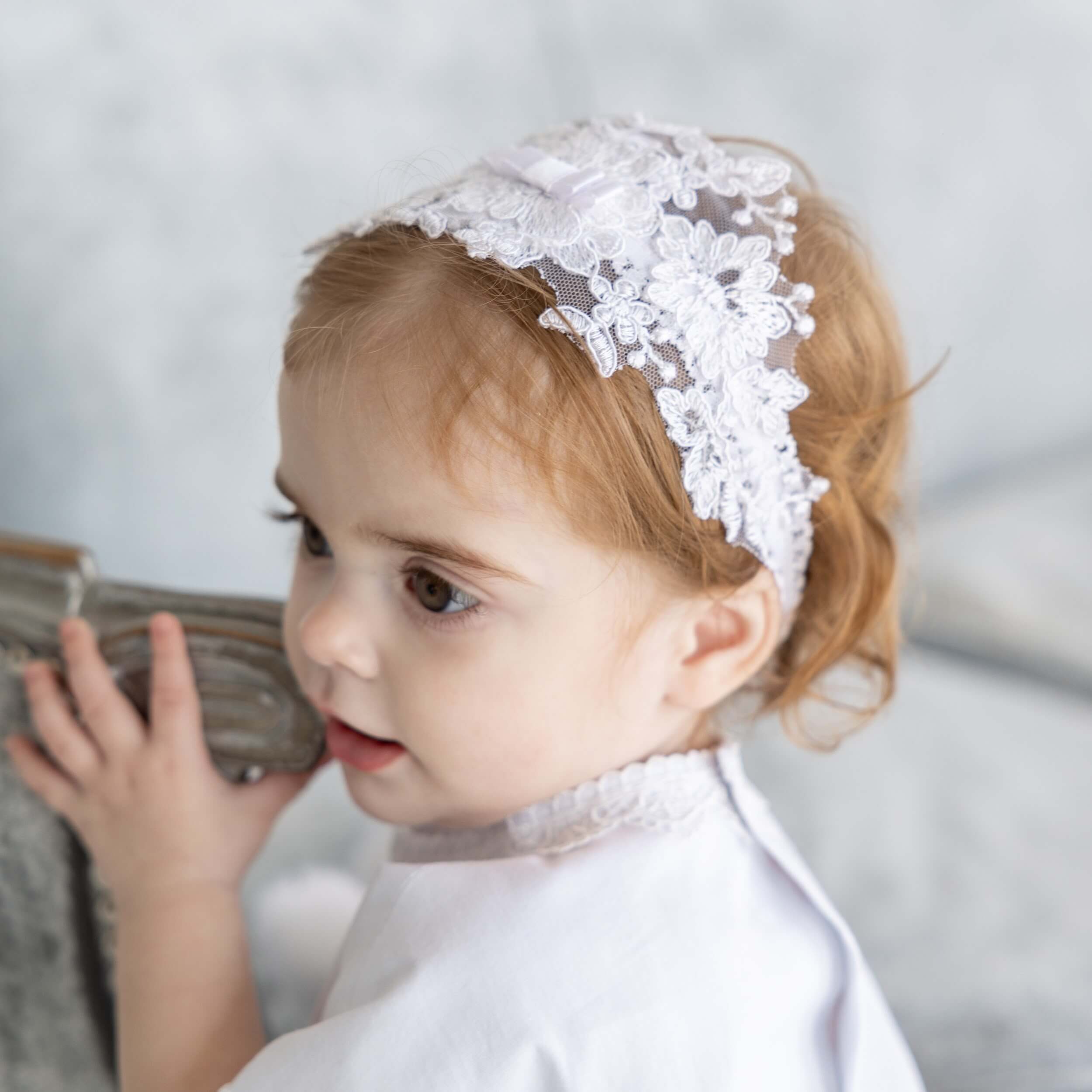 Child wearing a white babyheadband against a neutral background