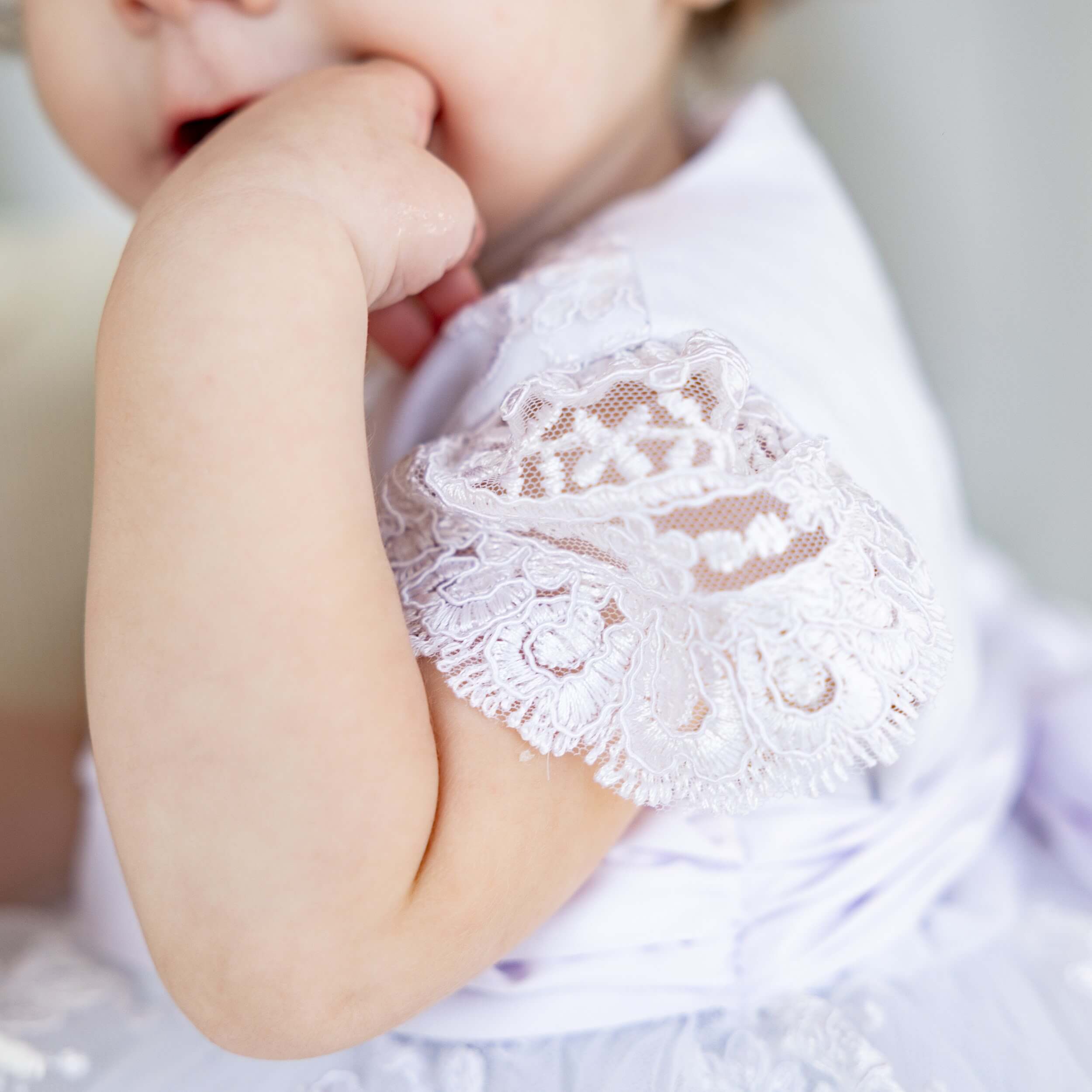 Close-up of a baby's hand wearing a Baptism Dress for Girls against a blurred background