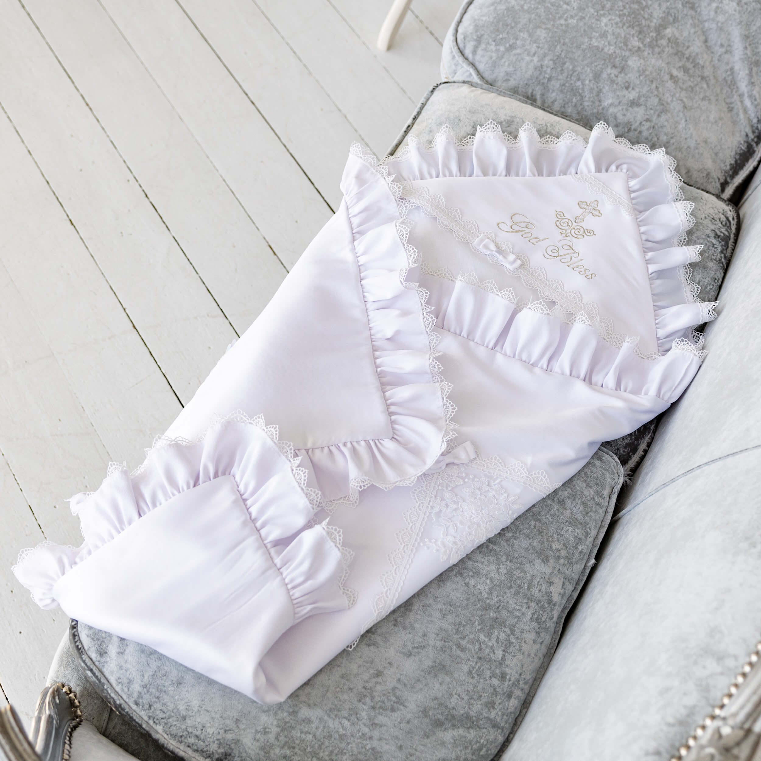 White baby baptism blanket with ruffles and embroidery on a gray surface