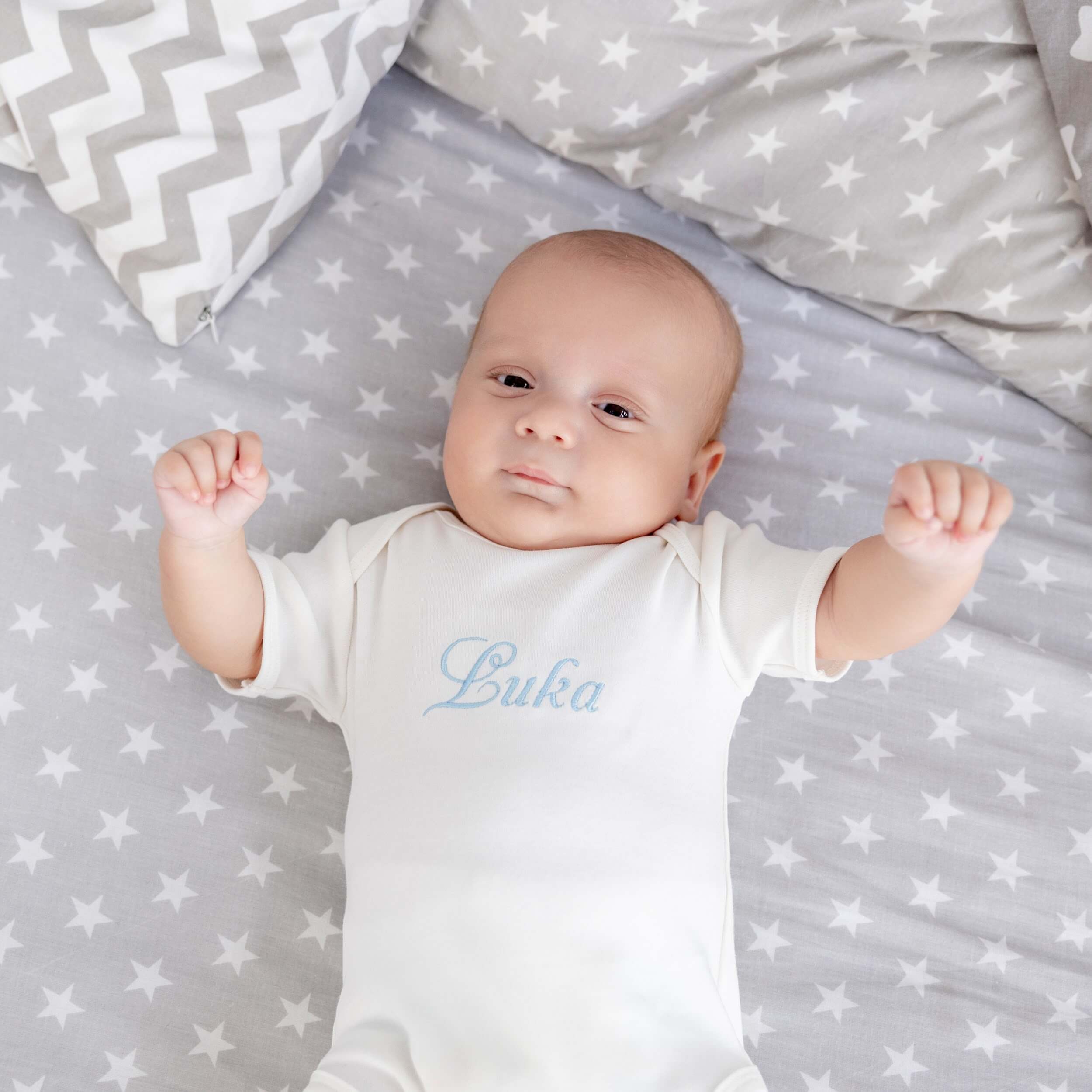 Baby lying on a star-patterned blanket wearing a Coming Home Bodysuit with blue text.