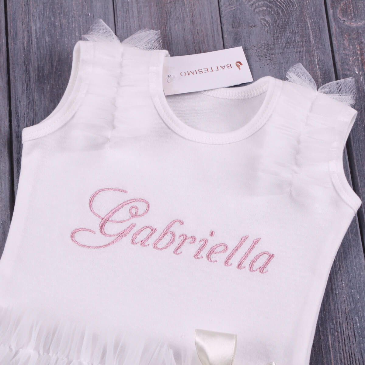 Coming Home Bodysuit with 'Gabriella' embroidery on a wooden surface