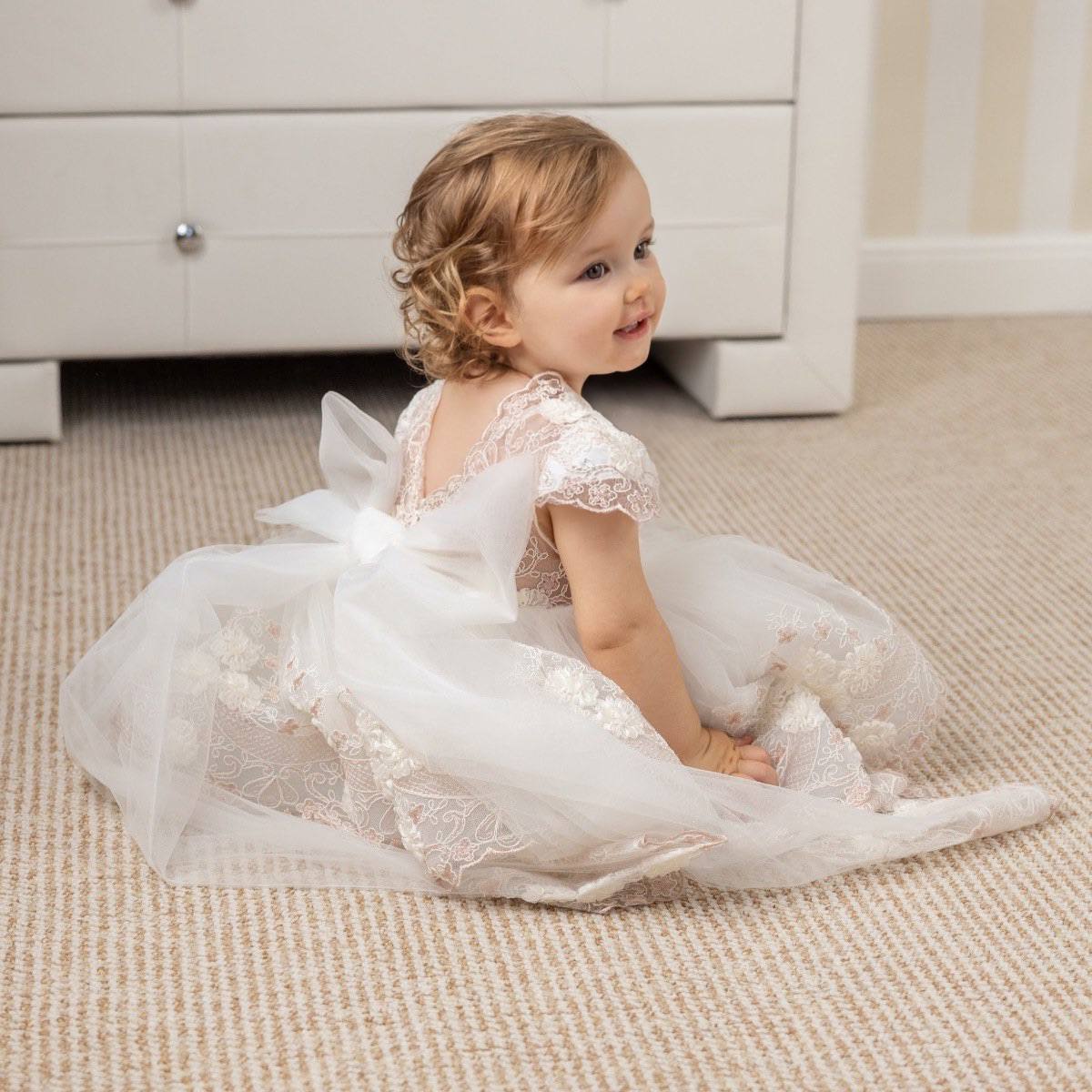 Child in a Baptism Dress with Detachable Train sitting on a carpeted floor.