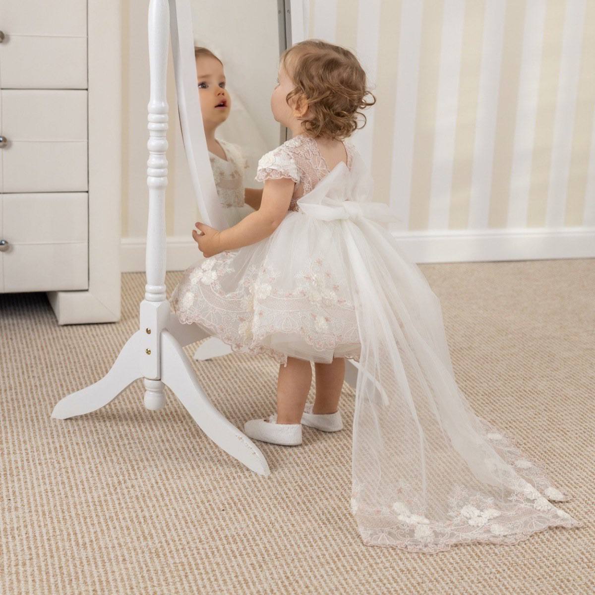 Child in a Baptism Dress with Detachable Train standing in front of a mirror.
