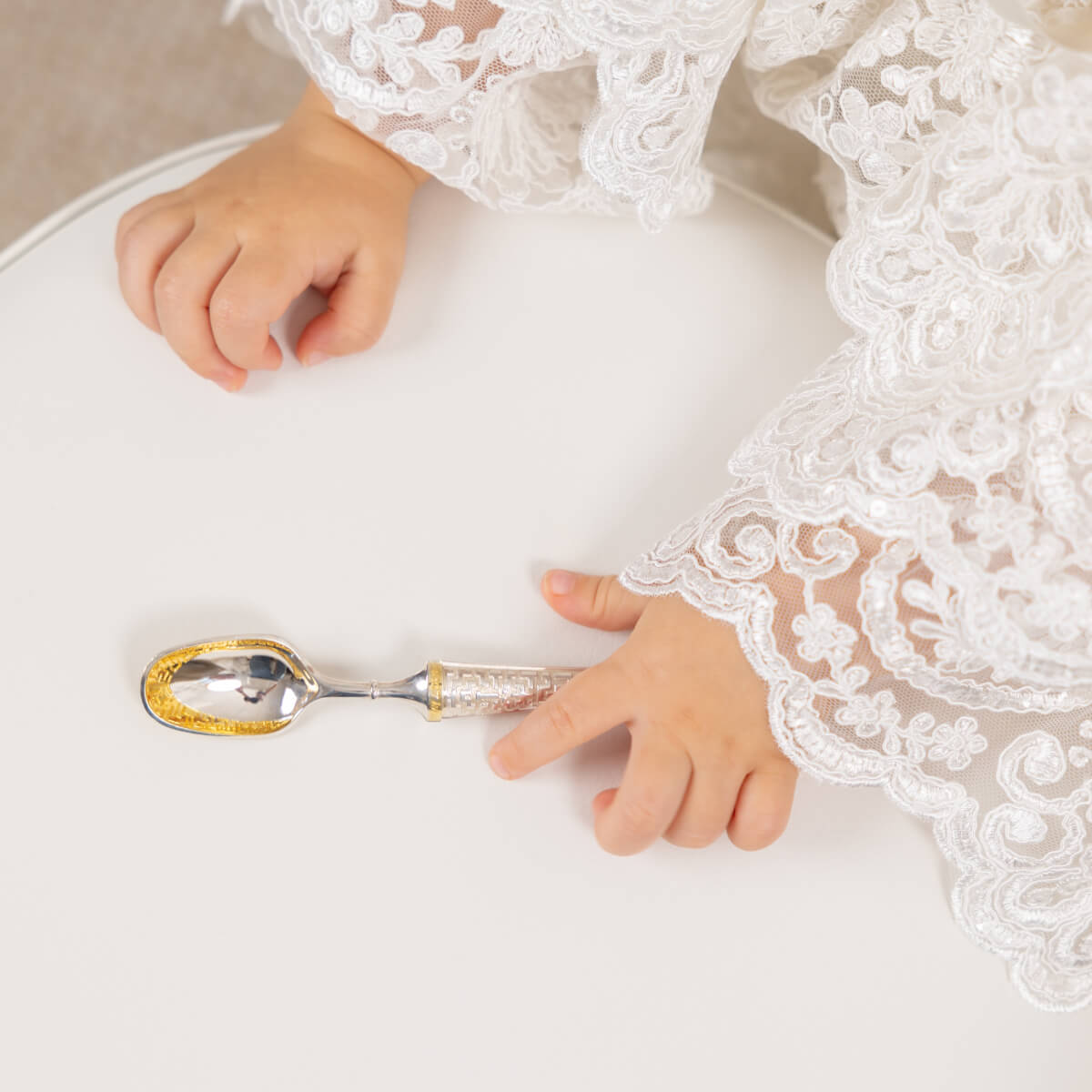 Child's hand reaching for a decorative spoon on a white surface with lace fabric.