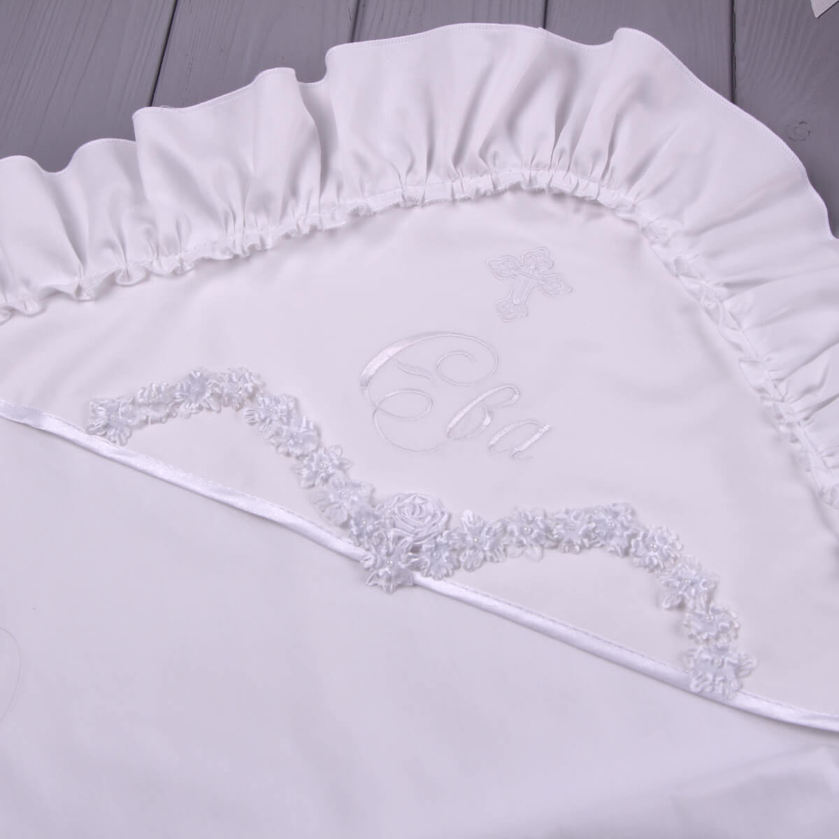 White ruffled christening blanket with decorative trim on a wooden surface