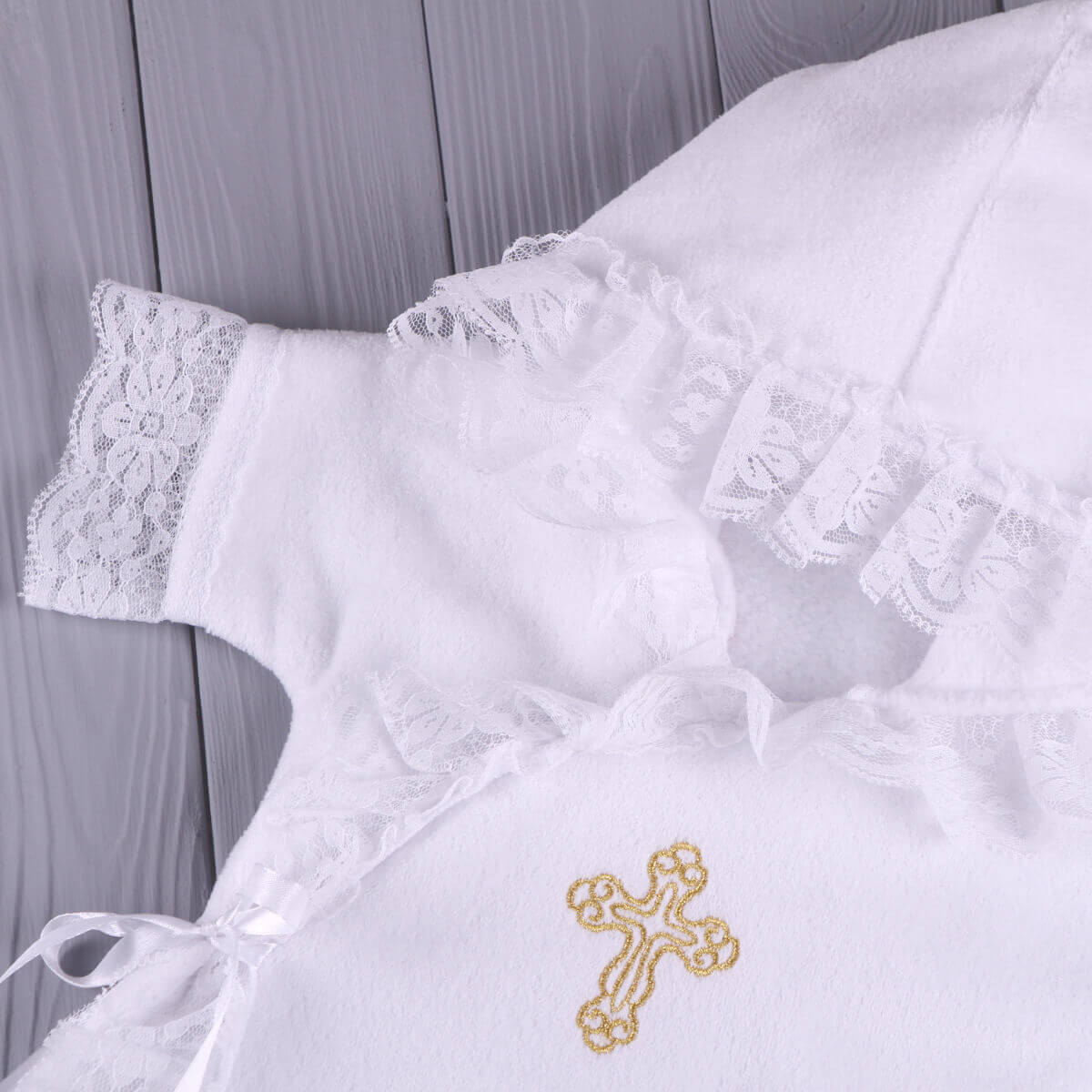 Baptism Gown with lace details and a gold embroidered cross on a wooden surface