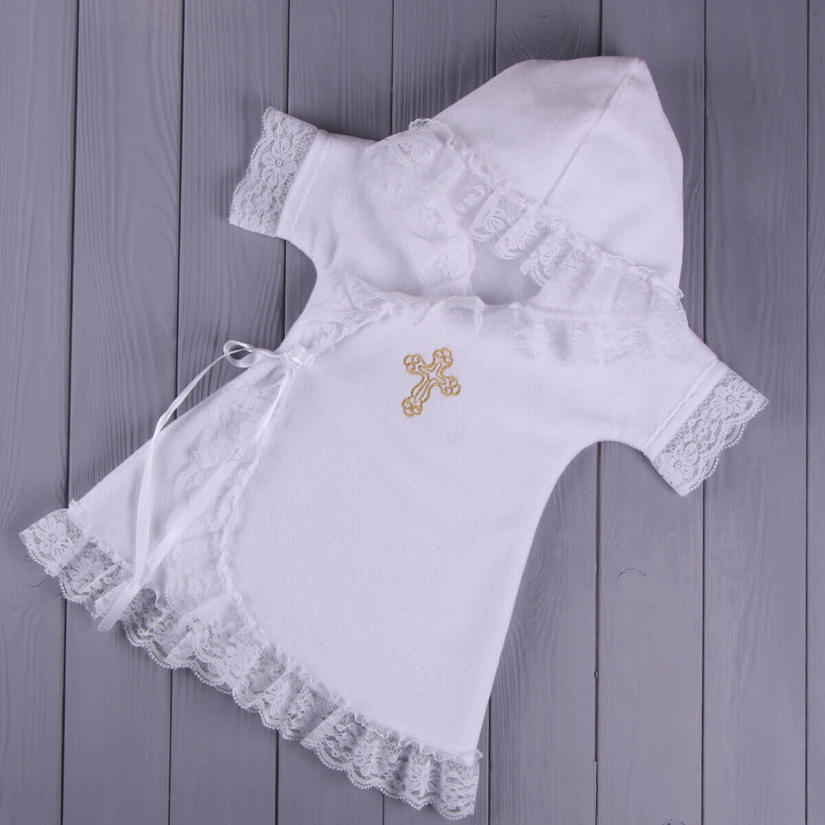 Baptism Gown with lace details and a gold cross on a wooden surface