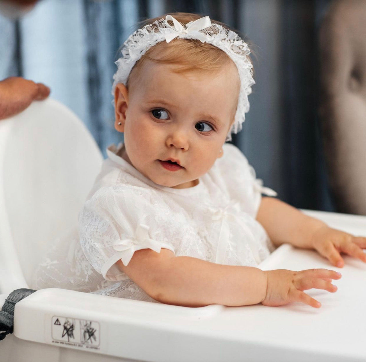 Baby in a Lace Baptism Gown Set with Bonnet for Girl with a lace headband sitting in a high chair.