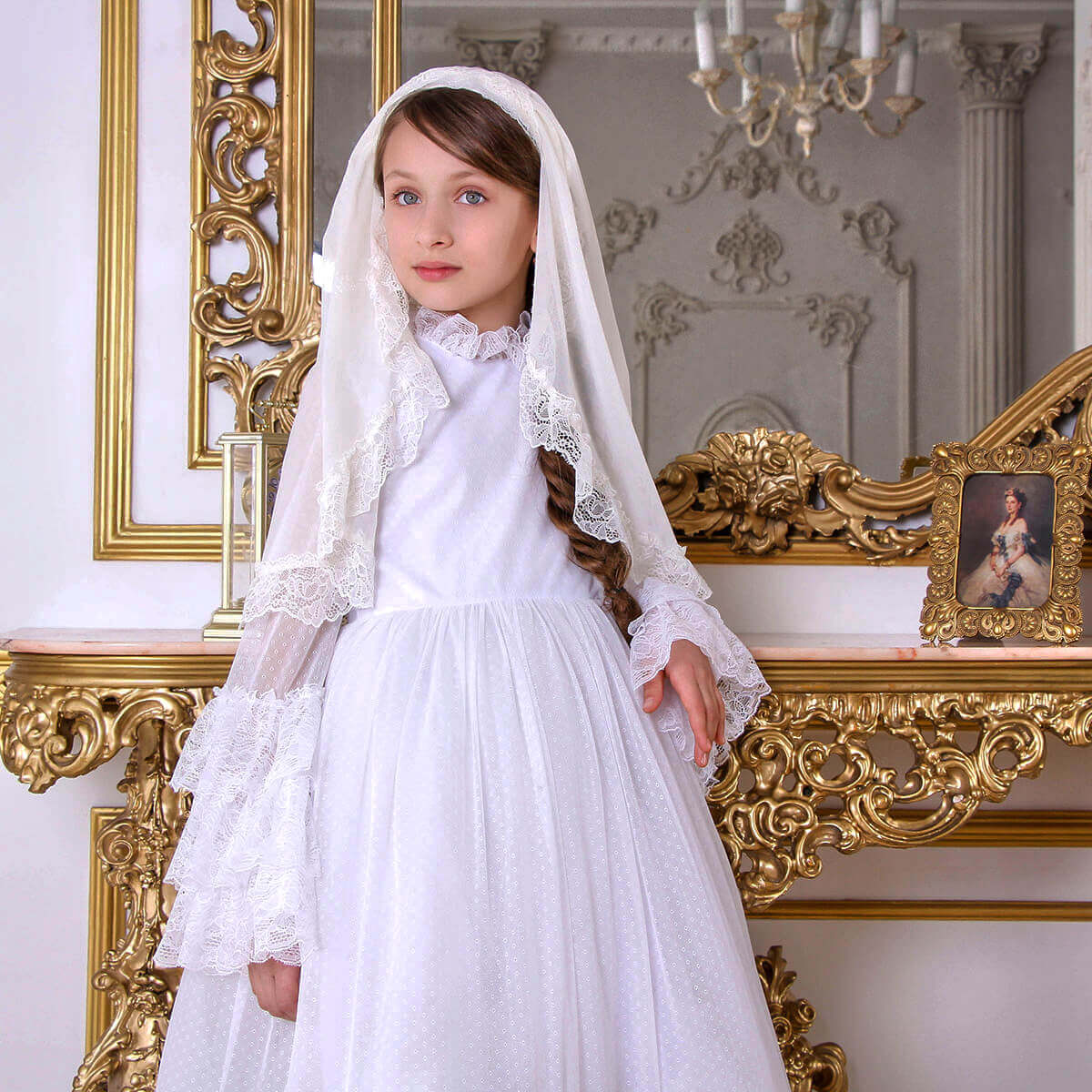 Young girl in a white dress with a veil standing in an ornate room.