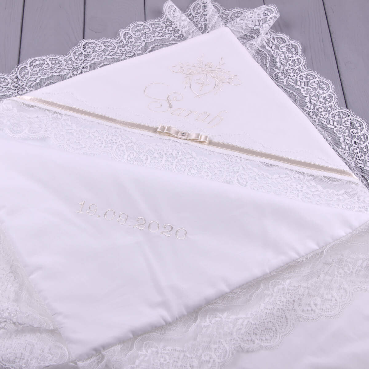 White christening blanket with lace trim on a wooden surface
